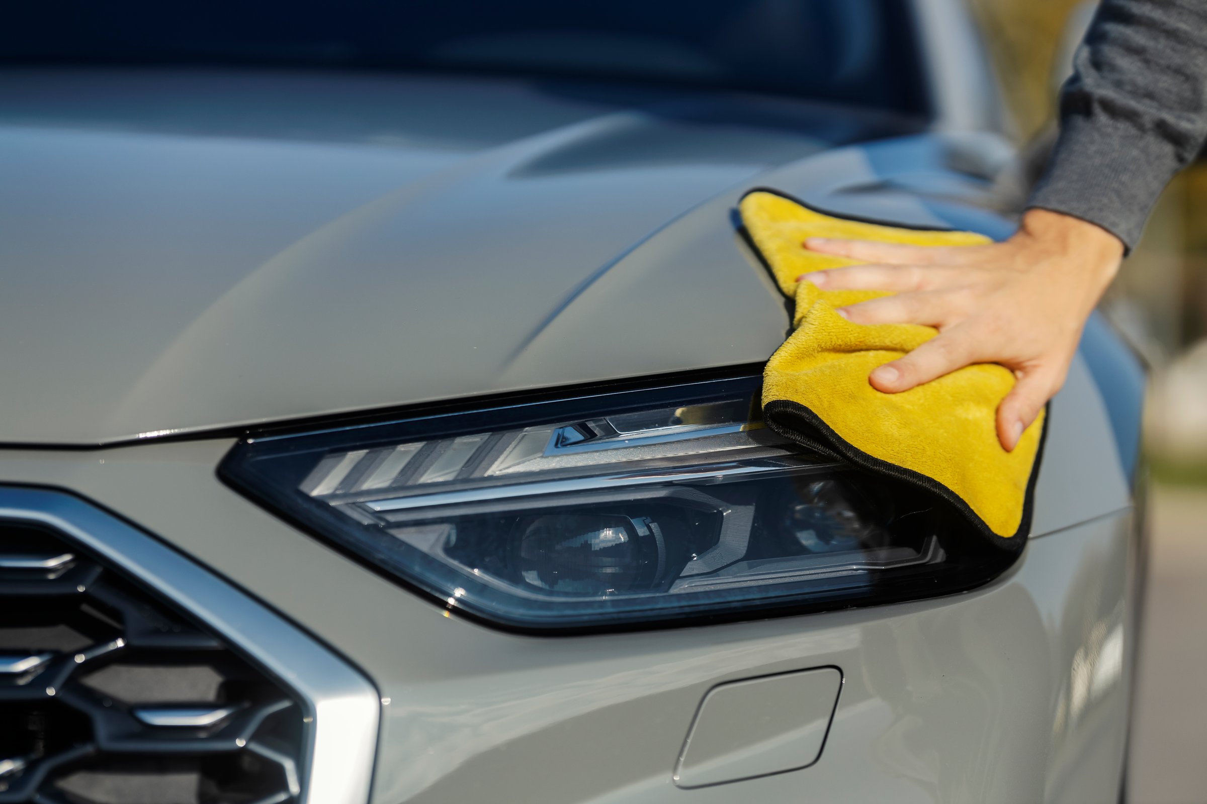 Cropped picture of man's hand polishing car headlights with microfiber cloth at self service car wash.