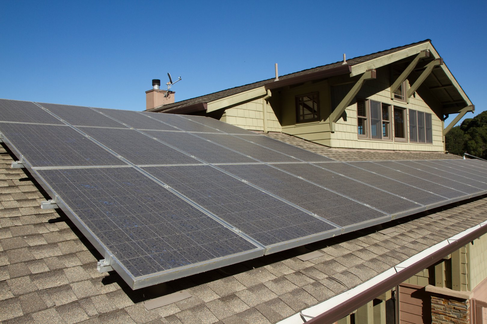 solar panels on roof of house. horizontal orientation, blue sky, gray panels on brown roof.