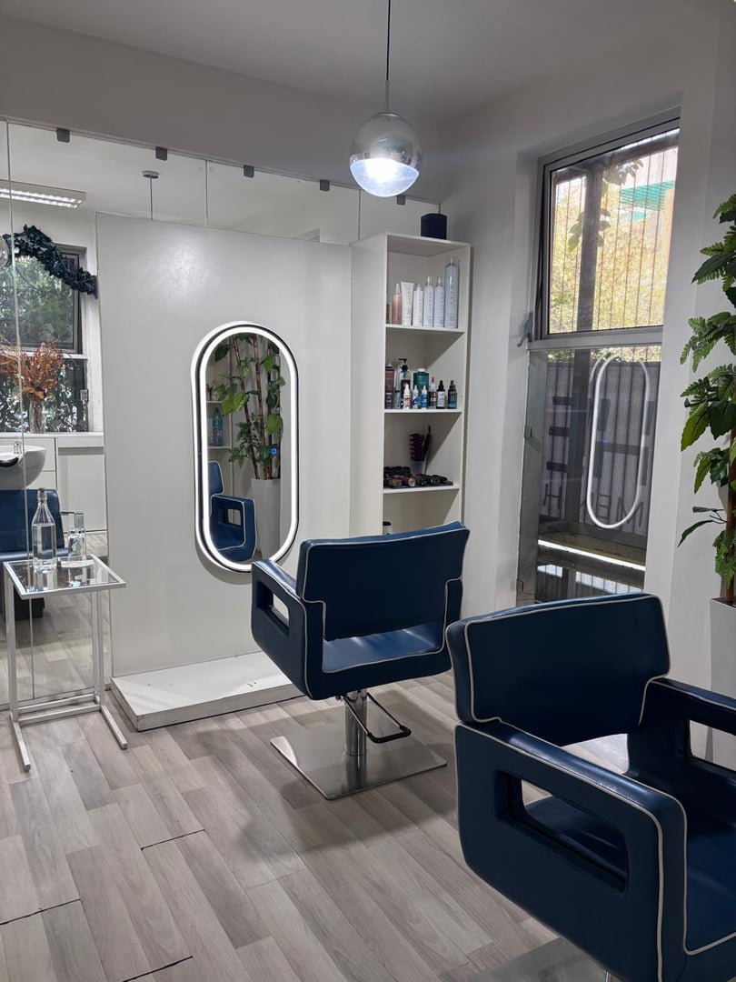 Modern hair salon with blue styling chairs, a mirror, and shelves with hair products in a bright interior.