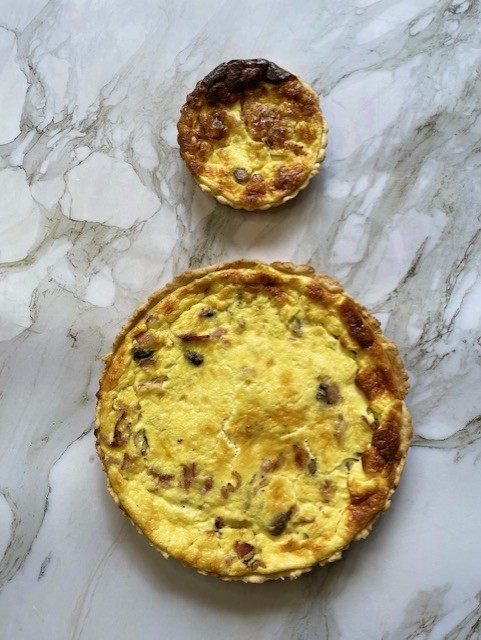 Two baked quiches, one large and one small, with golden-brown tops, on a marble surface.