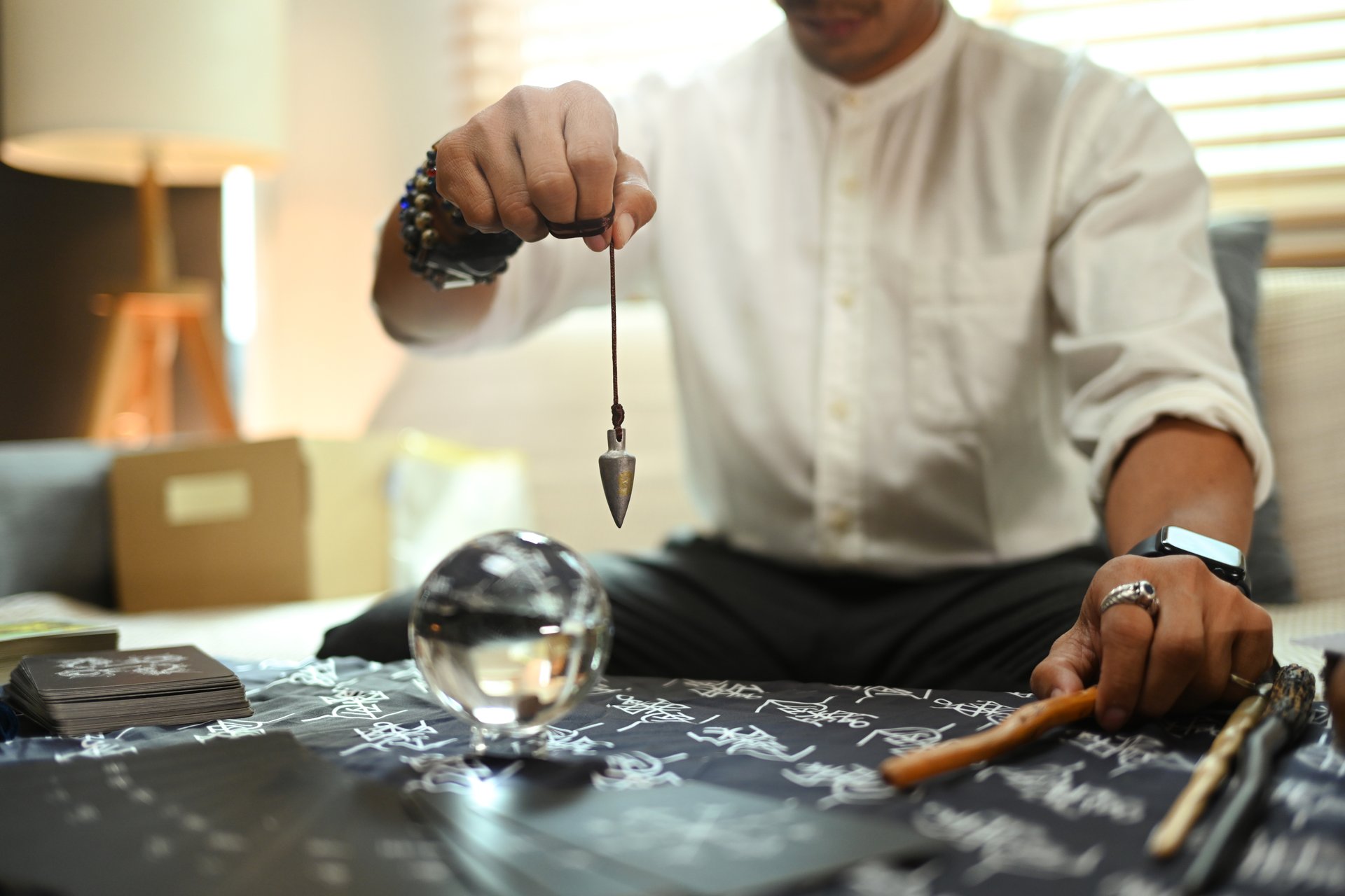 Mysterious fortune teller holding an iron pendulum forecasting over crystal ball. Divination concept.
