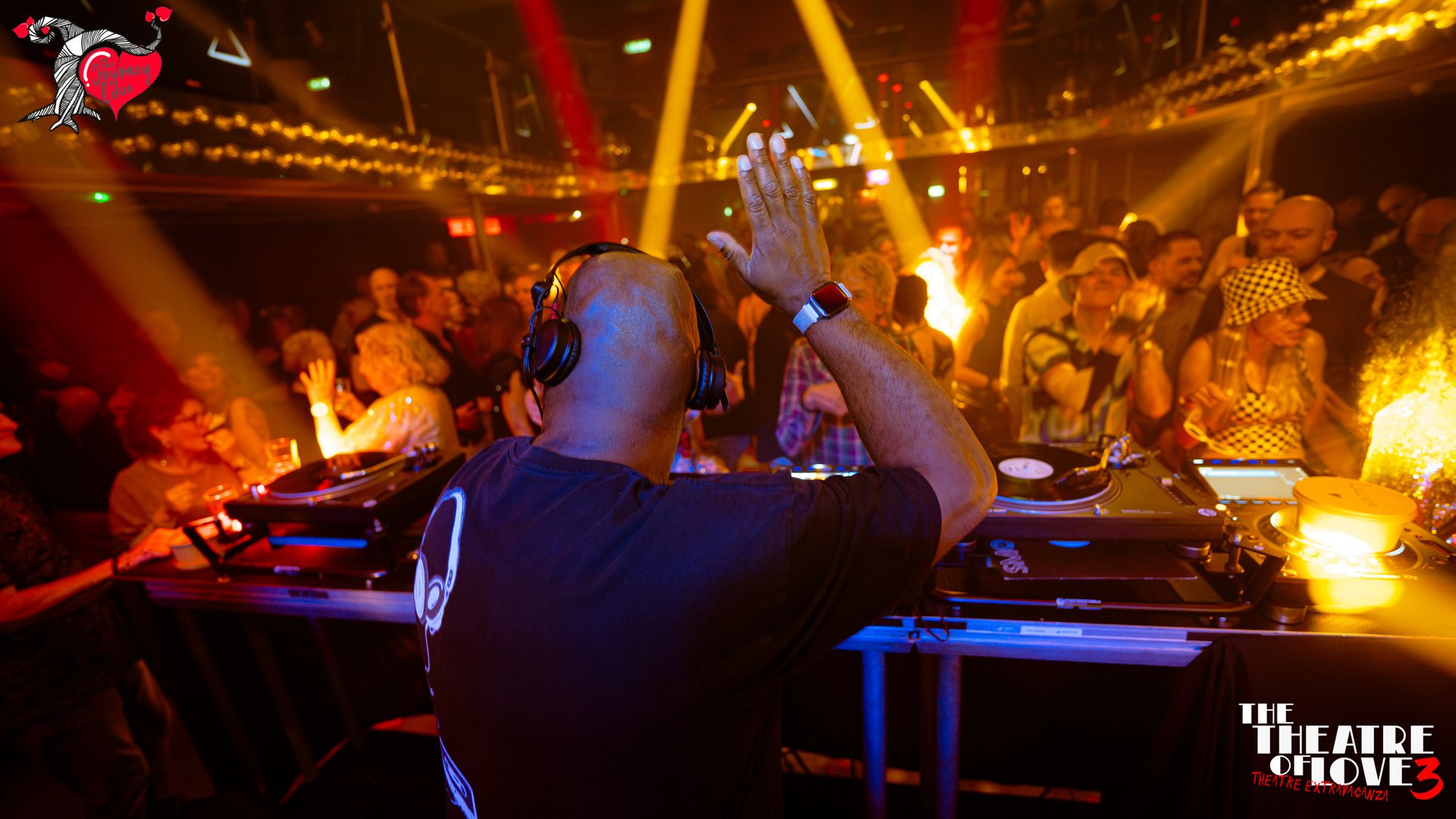 DJ spins records at a lively nightclub with a vibrant crowd and colorful lights, logo in the corner says The Theatre of Love.