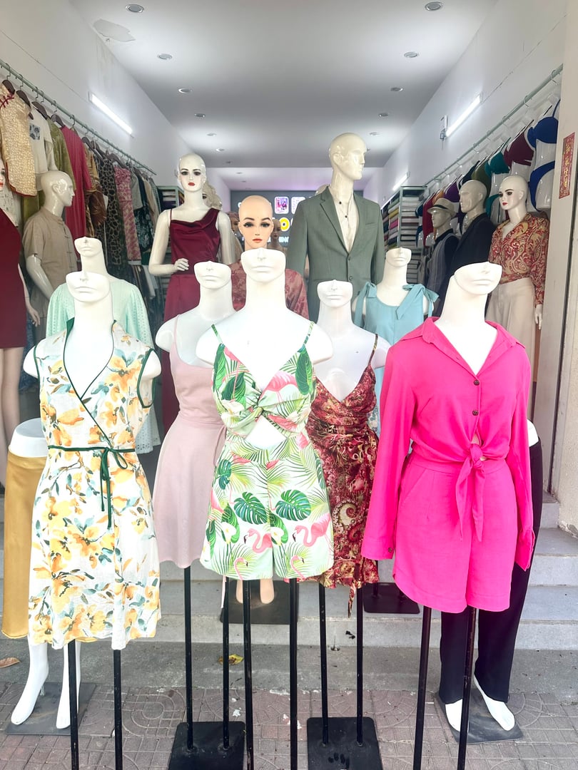 Mannequins display colorful women's clothing ensembles in a boutique, with a suit-clad mannequin in the background.