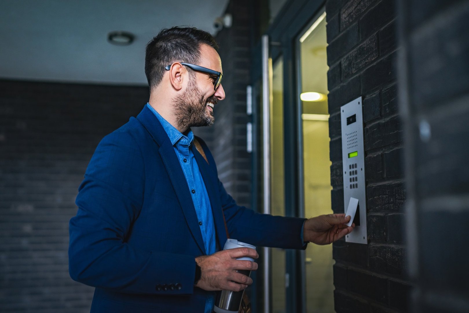 Adult man in a blue suit use an access card at a company door entry system, smiling. The scene is well-lit, suggesting a modern, professional setting