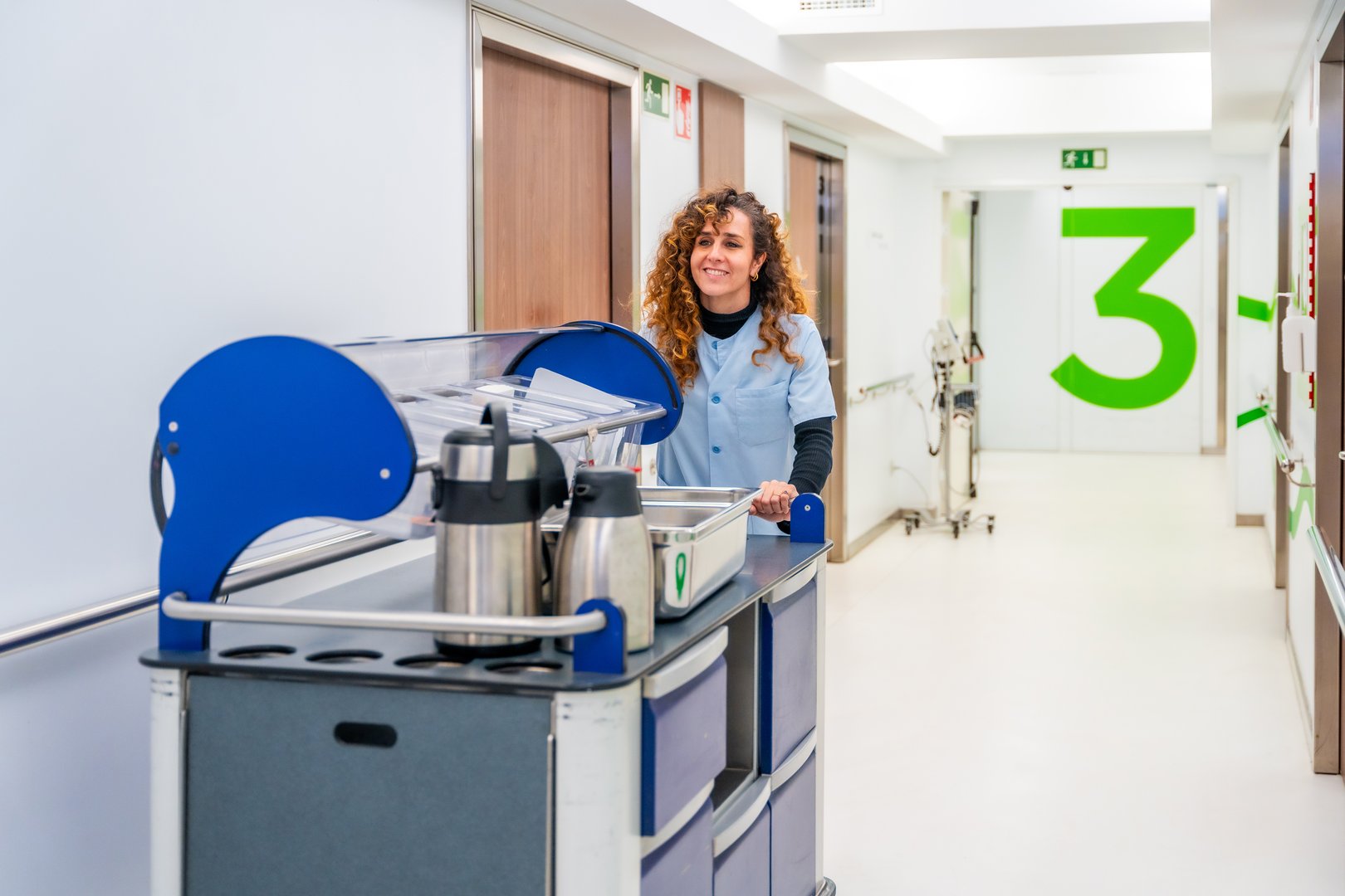 Happy nurse carrying coffee with a trolley along hospital in the morning