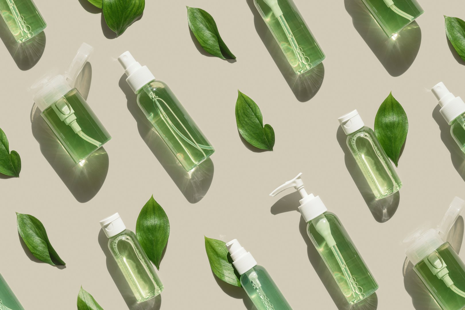 Natural Organic Cosmetic products with green liquid and leaves for skin treatment, beauty routine, skin health. Minimal top view pattern with lotion, tonic, gel, micellar water mockup with sun shadows