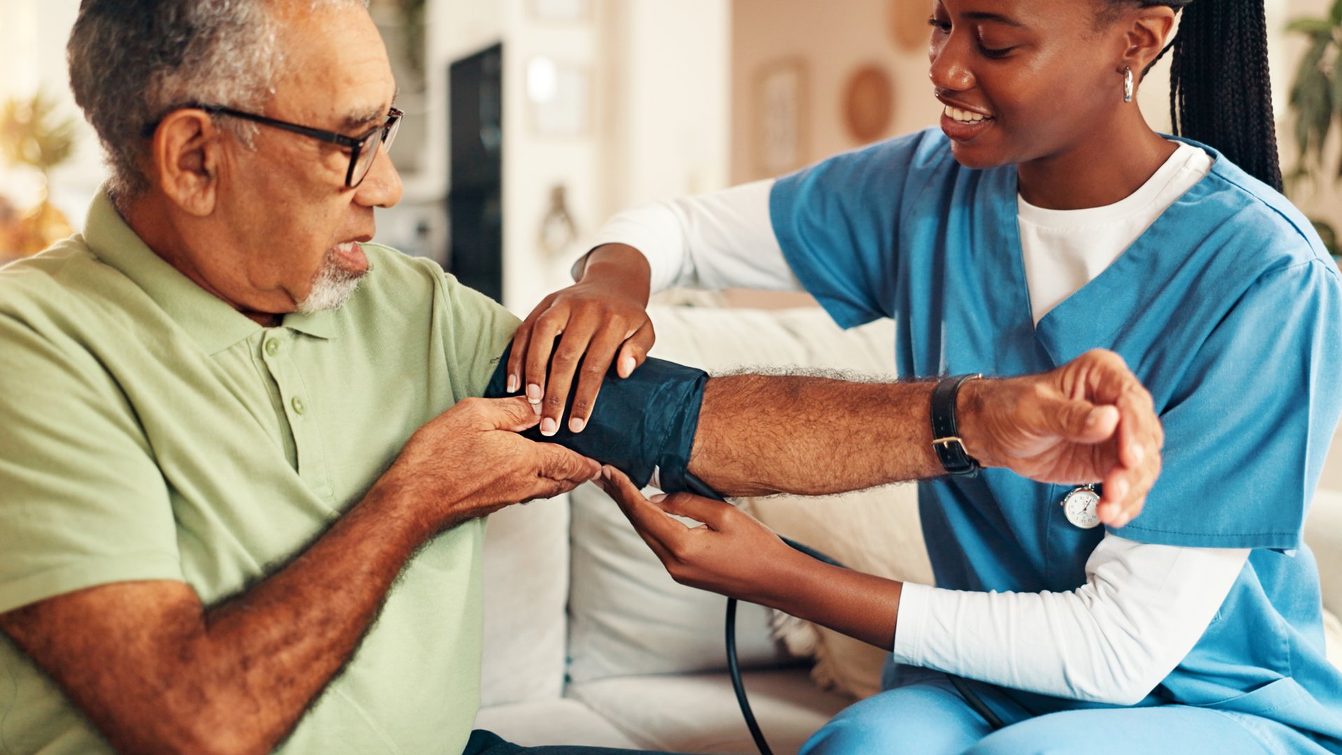 Senior man, nursing home and blood pressure check with nurse, medical care and health exam on arm. Living room, diagnosis and conversation with healthcare, wellness support and monitoring or test