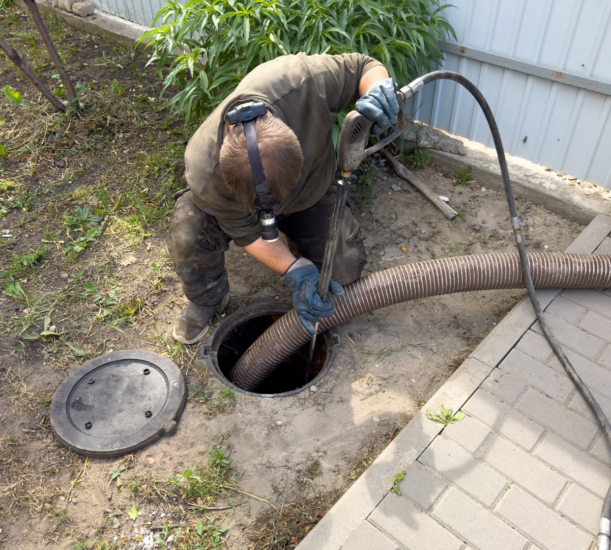 A man is working on a sewer line wearing a hard hat and gloves