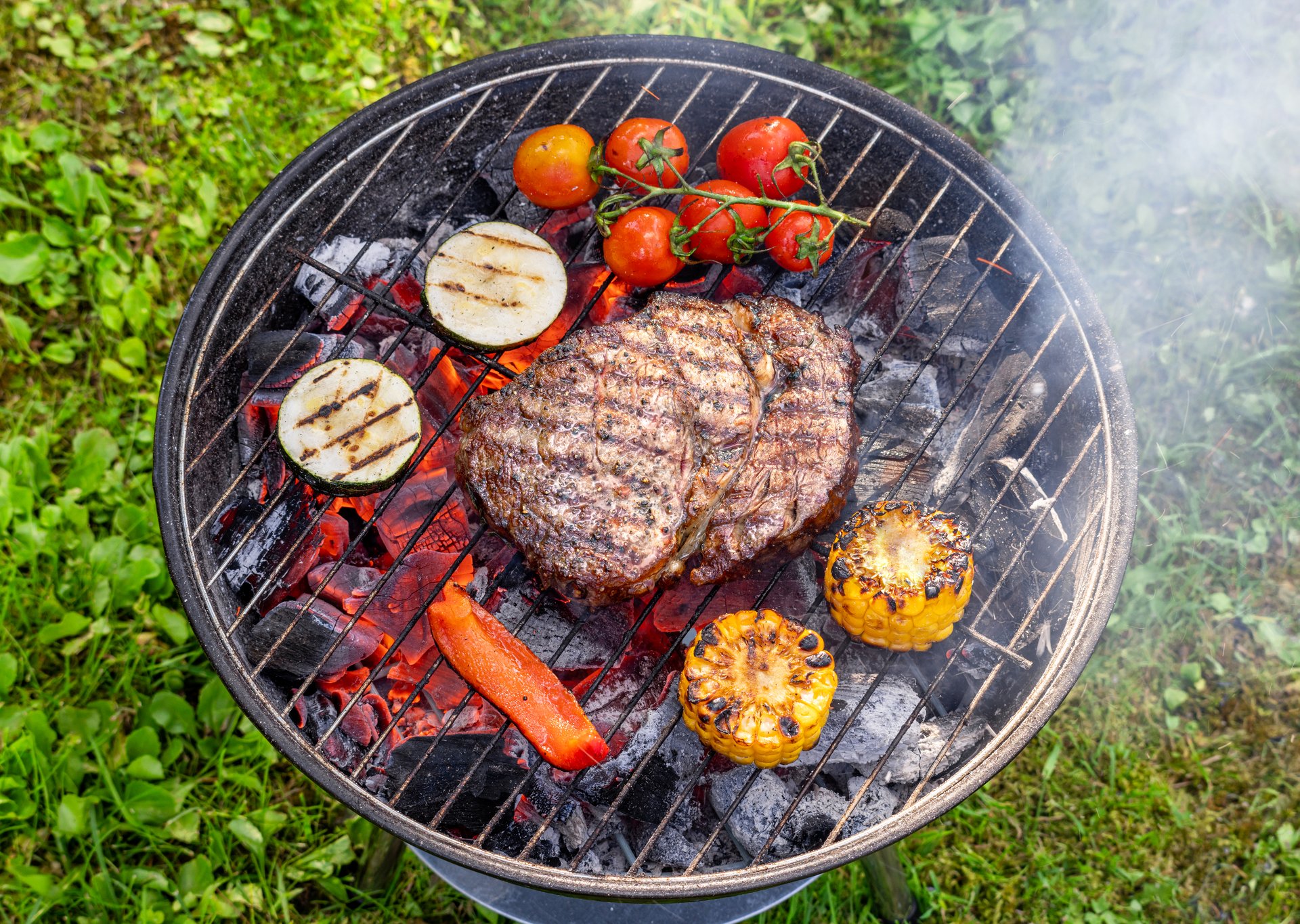 beef steak and vegetables on charcoal grill, top view