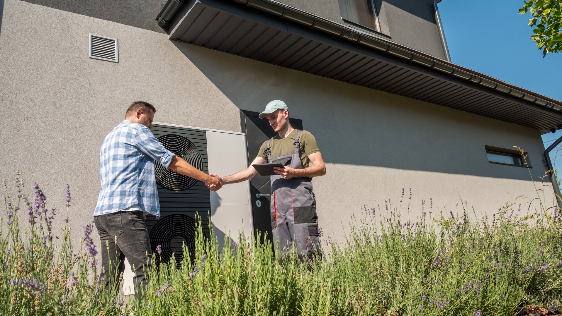 A technician and a homeowner discussing heat pump maintenance outside a house, with a heat pump unit visible in the background. High quality photo