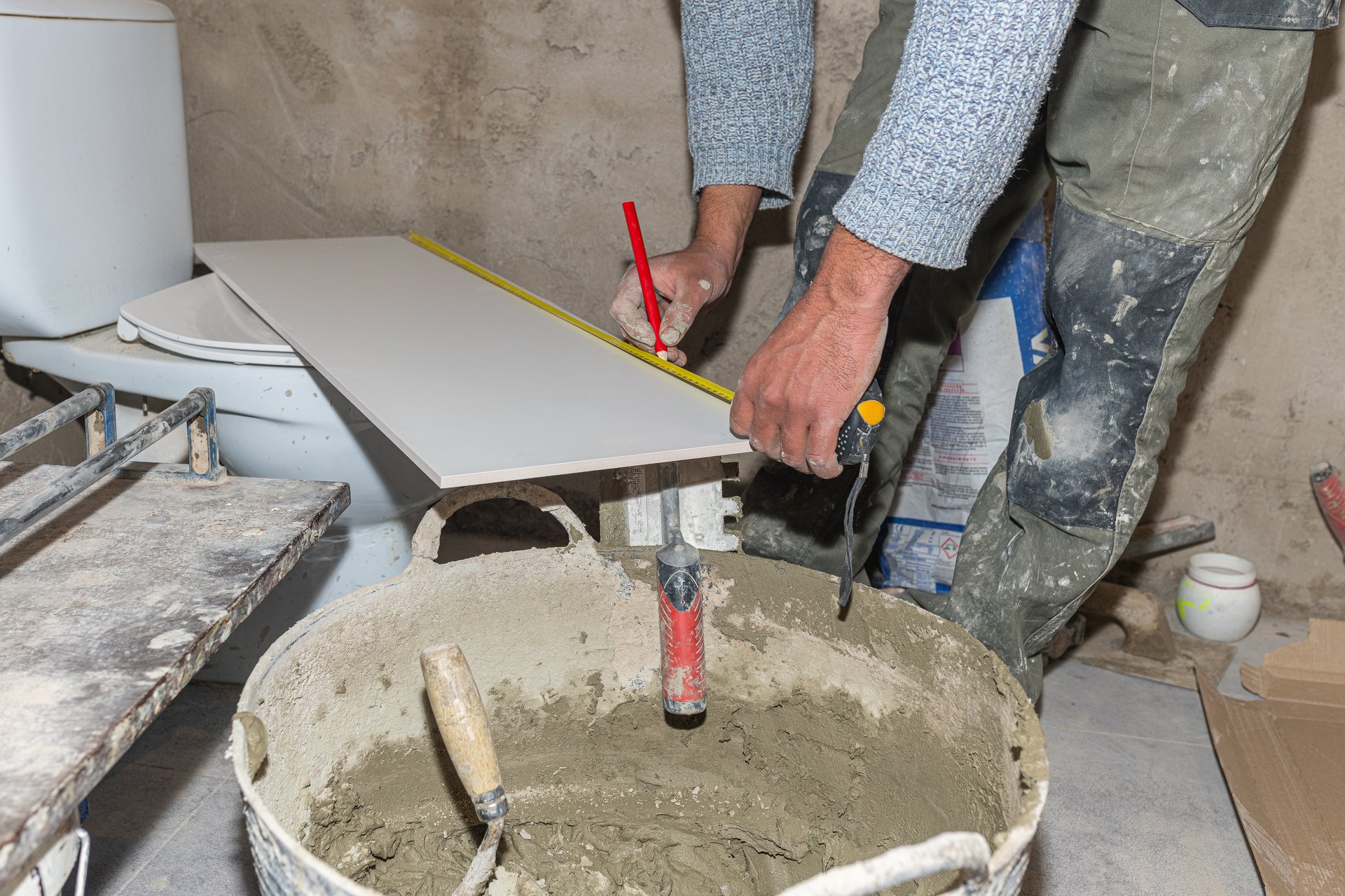 Tiler measuring a ceramic tile with a tape measure and marking it with a pencil during bathroom renovation