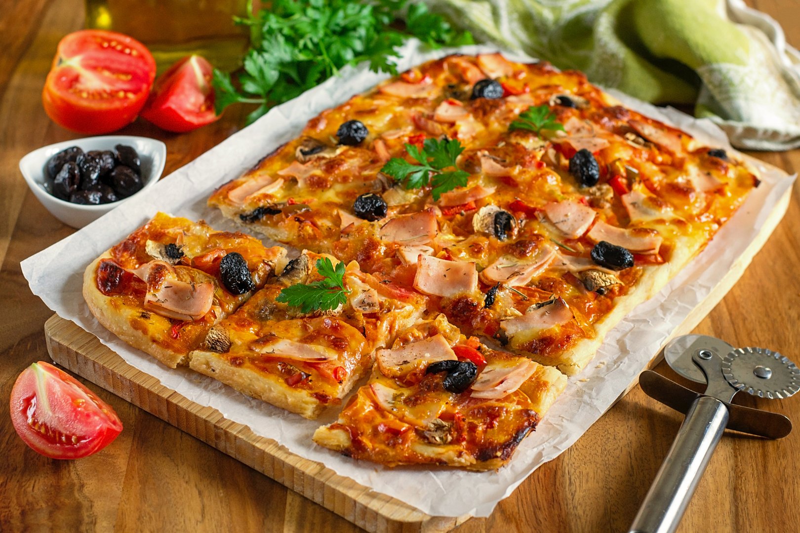 Fresh homemade rectangular pizza with ham, tomatoes, cheese and olives