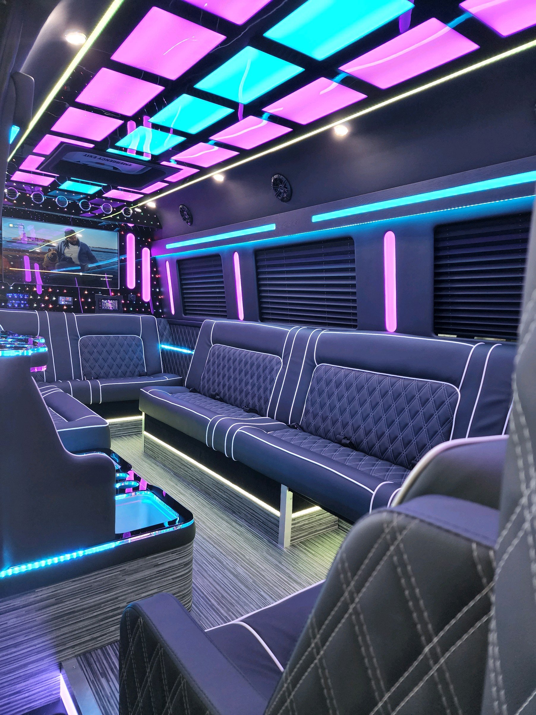 Interior of a luxury party bus with colorful LED lights, quilted leather seating, and a modern entertainment system.