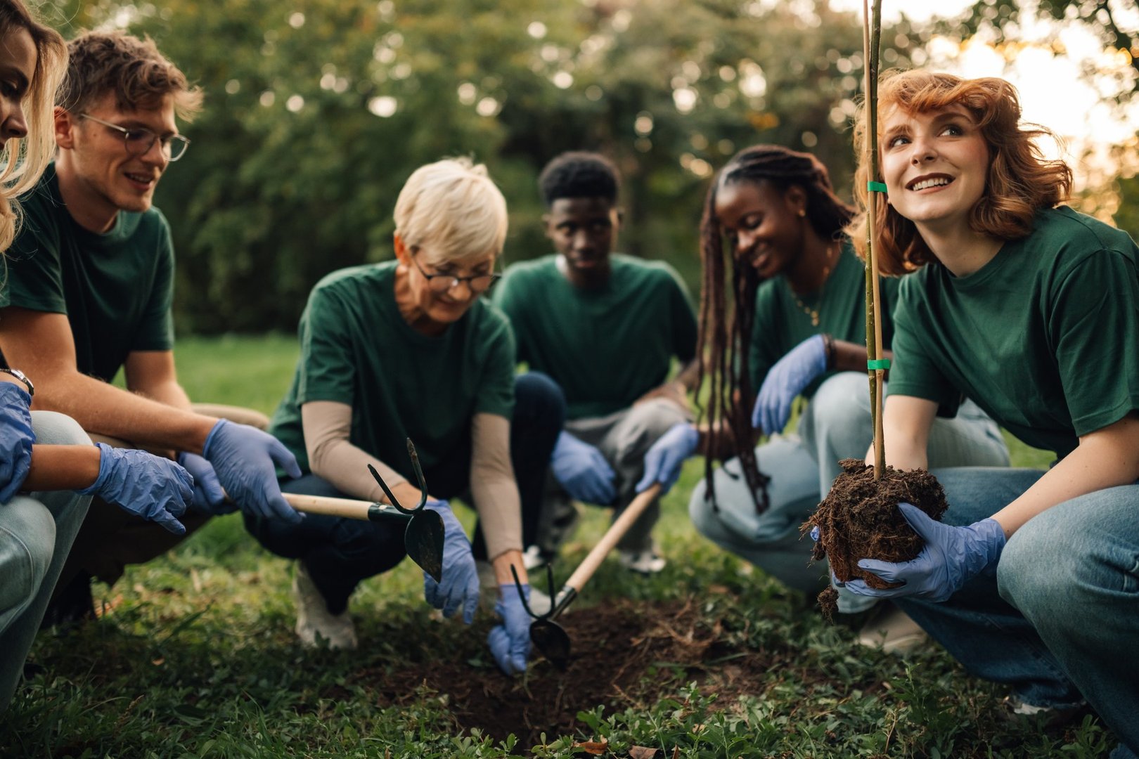 Volunteers of all ages happily plant a tree in a sunny park, showing commitment to a greener future. Community teamwork promotes eco friendly practices and conservation on earth day