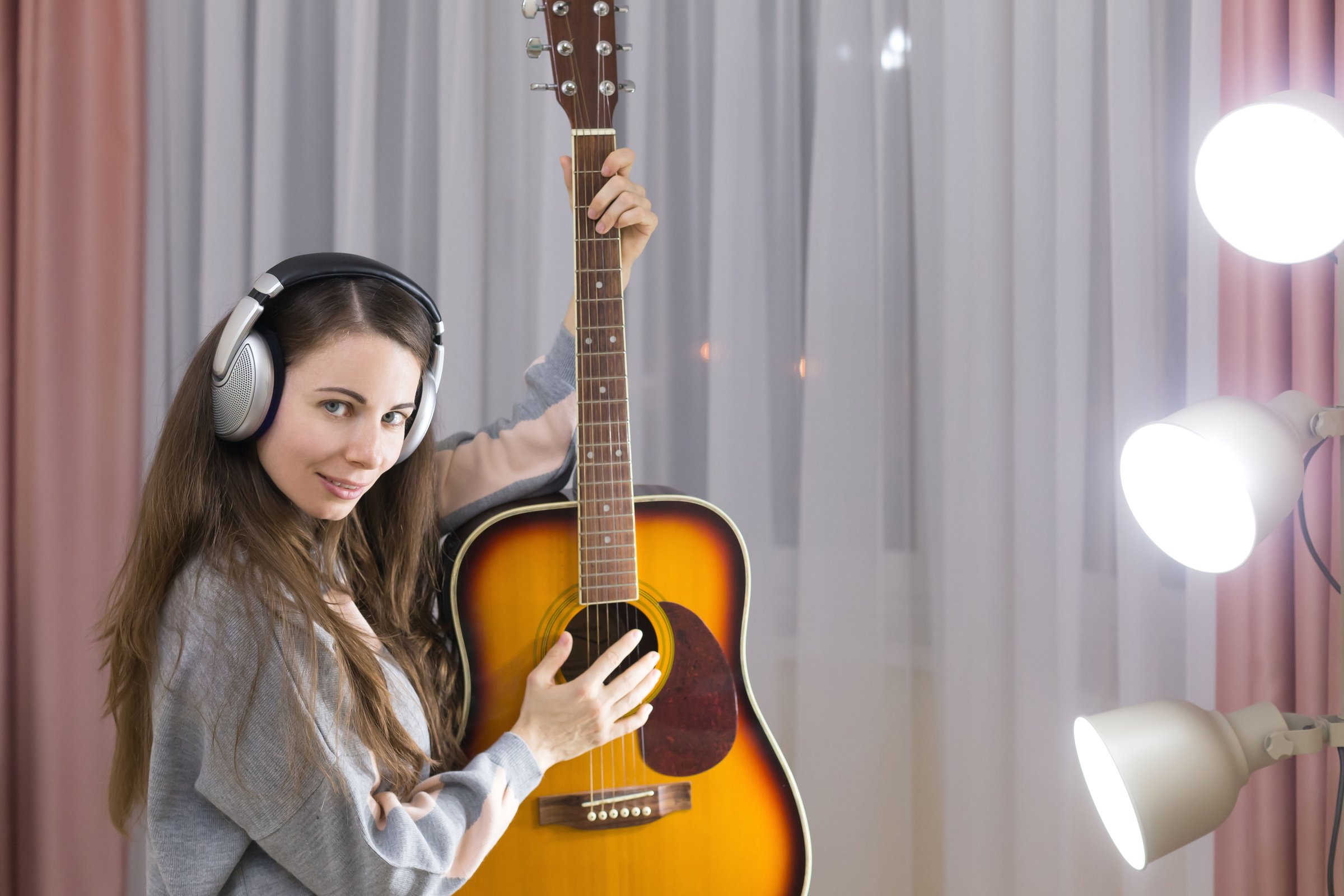 Beautiful brunette woman playing guitar, listening to music headphones, sings a song. Female happy hobby. Acoustic instrument concept. Fashion urban style.