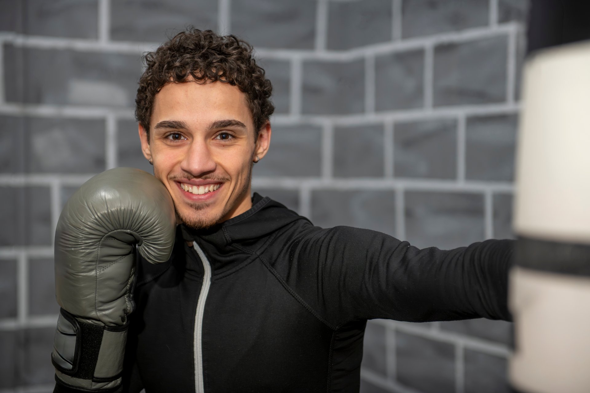 Young boxer smiling while training with a punching bag in the gym, showcasing skill and determination in boxing gloves