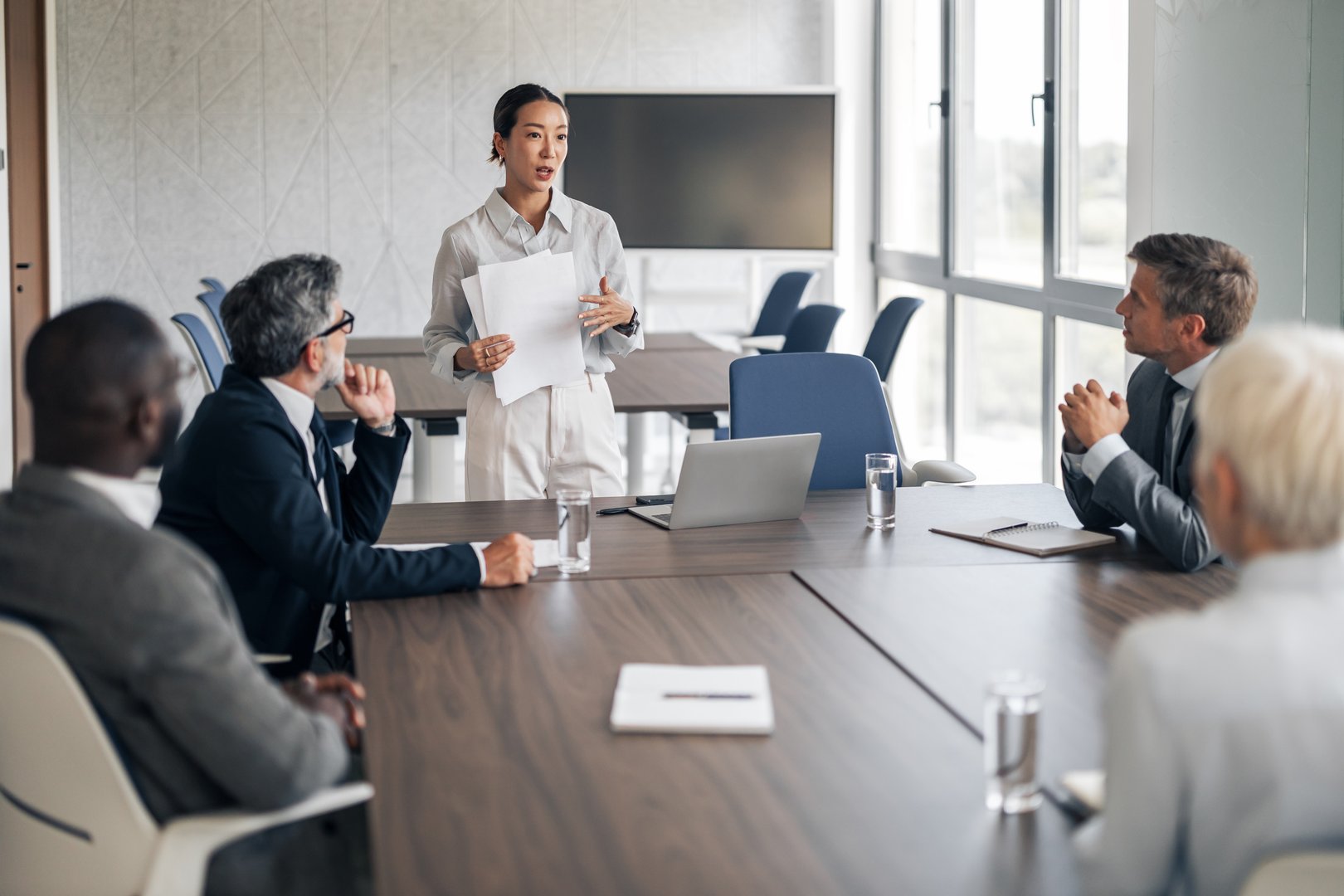 Businesswoman presenting important documents during a corporate meeting, engaging with diverse colleagues listening intently around a conference table in a modern office