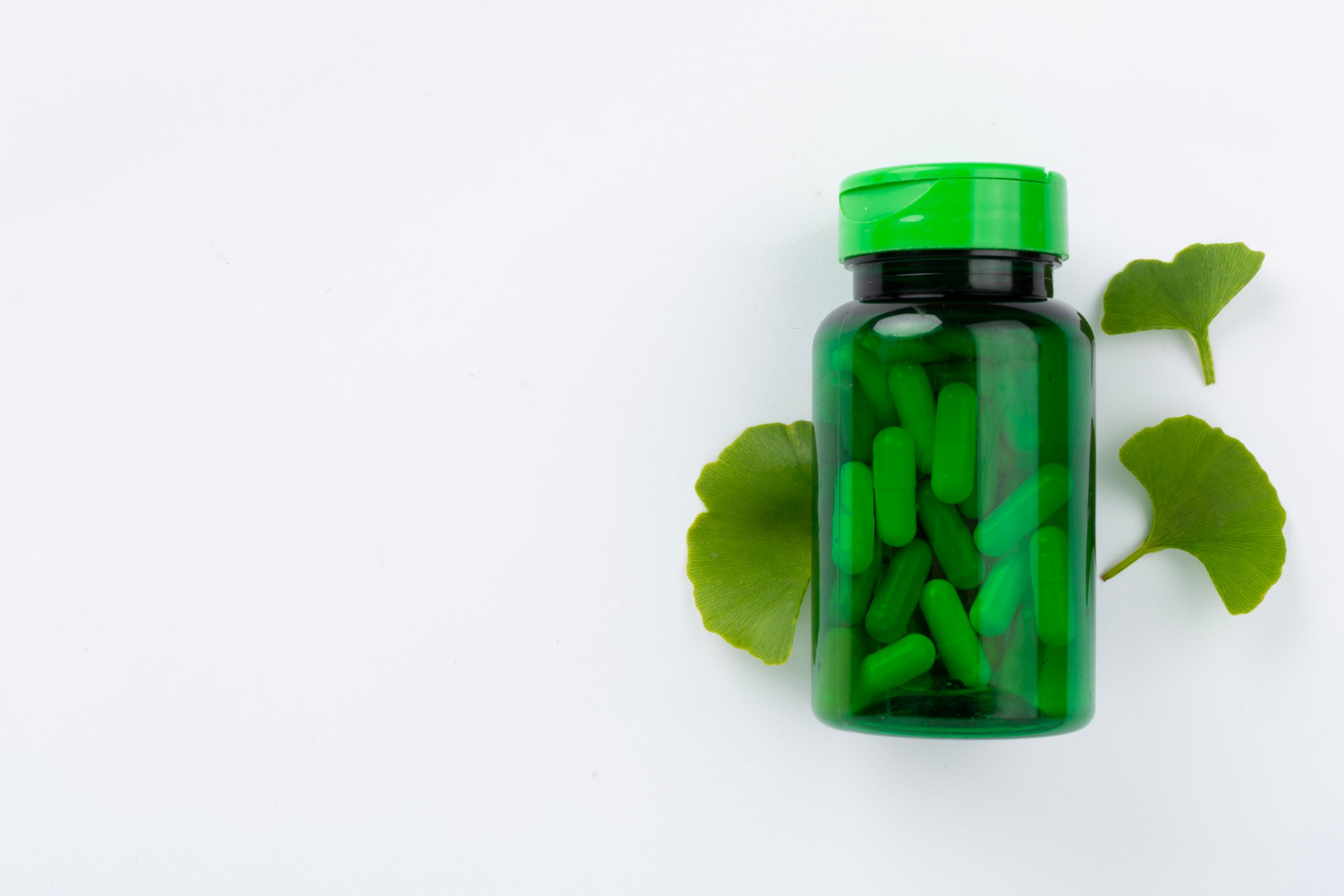 Ginkgo leaf with bottle of pills on color background, top view