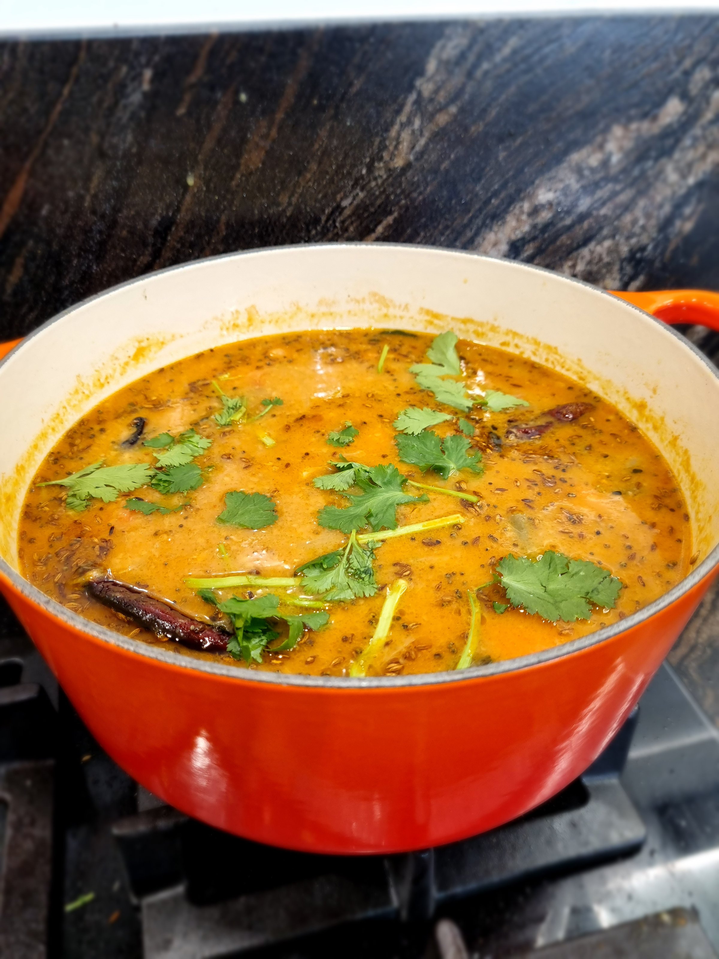 A pot of dal tadka with coriander garnish, cooked in a red pot on a stove.