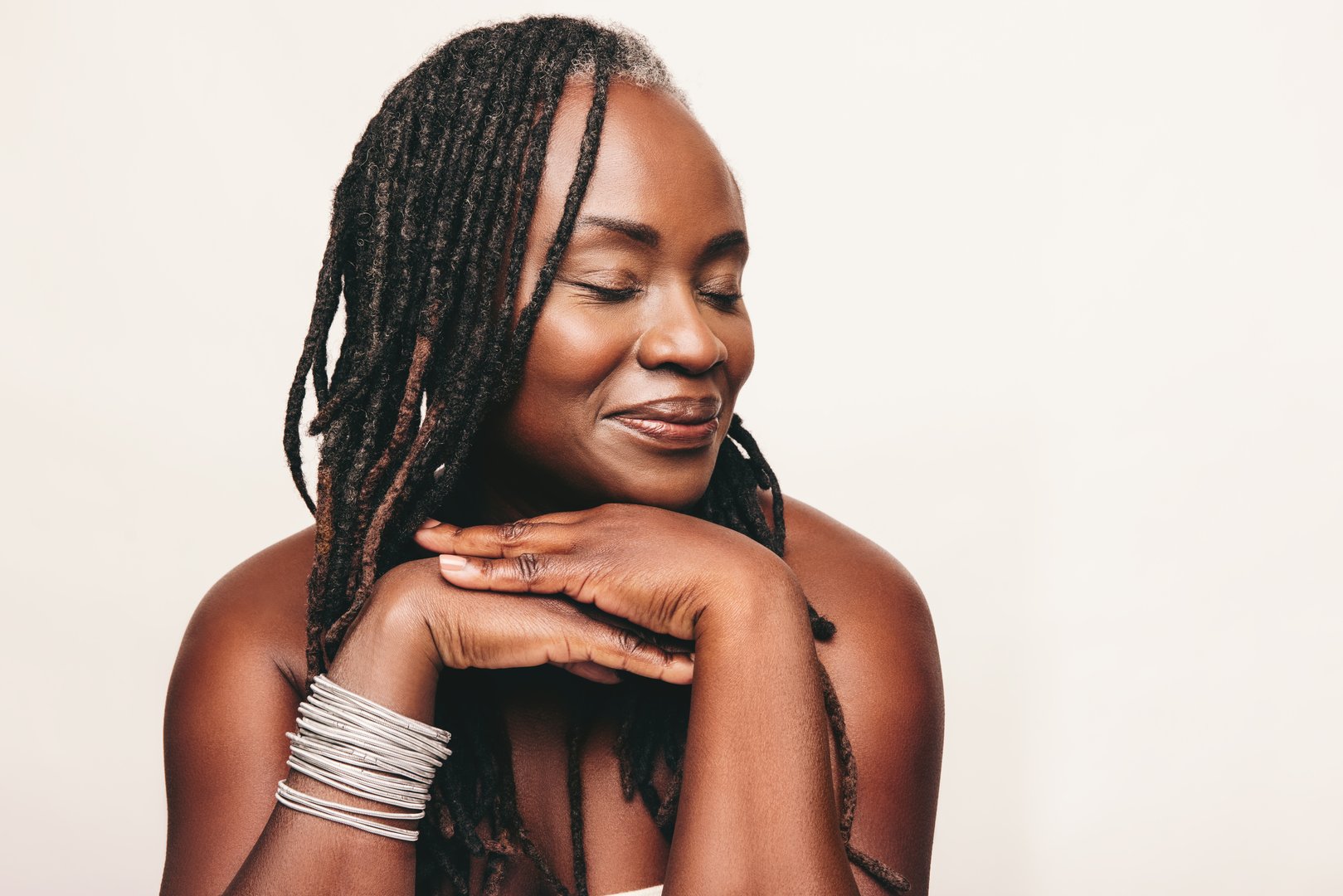 Beautiful woman with dreadlocks smiling with her eyes closed in a studio. Mature woman wearing light make-up against a white background. Happy middle-aged woman pampering her ageing body.