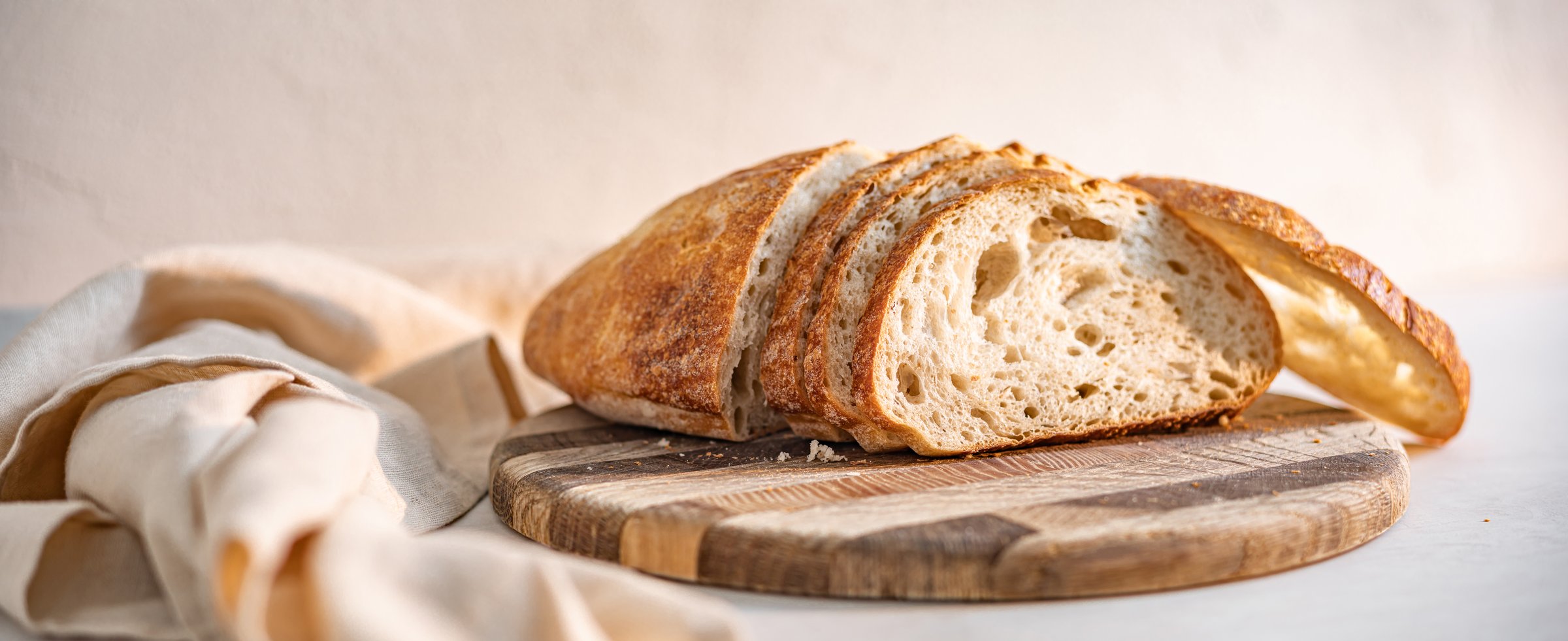 A loaf of freshly sliced sourdough bread on a wooden board, with a cloth beside it.