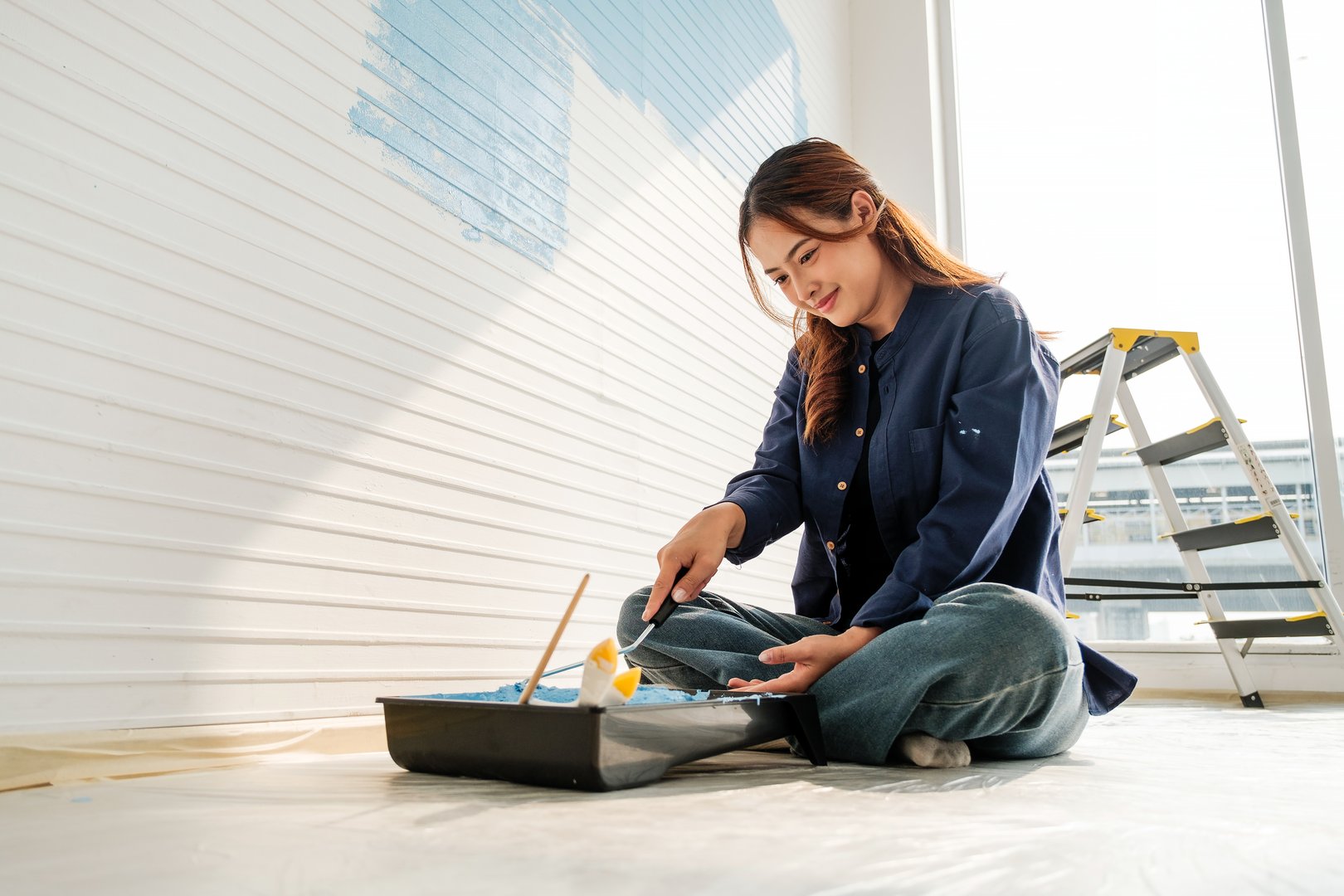 Happy couple is having fun while painting the walls of their new apartment using paint rollers