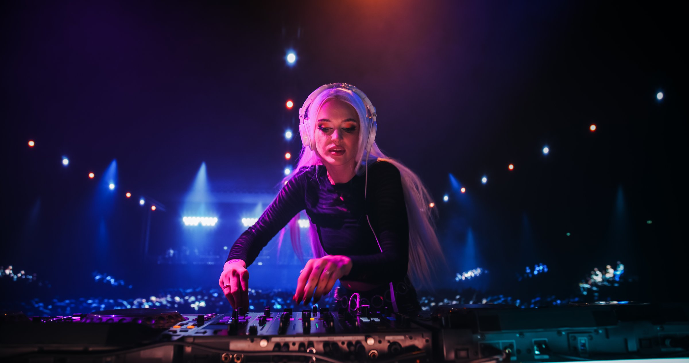 Dance Music Artist Performing a DJ Set on Stage in a Nightclub, Standing Behind Turntables and Under a Neon Concert Setting with Cinematic Lighting and Excited Audience in an Underground Venue