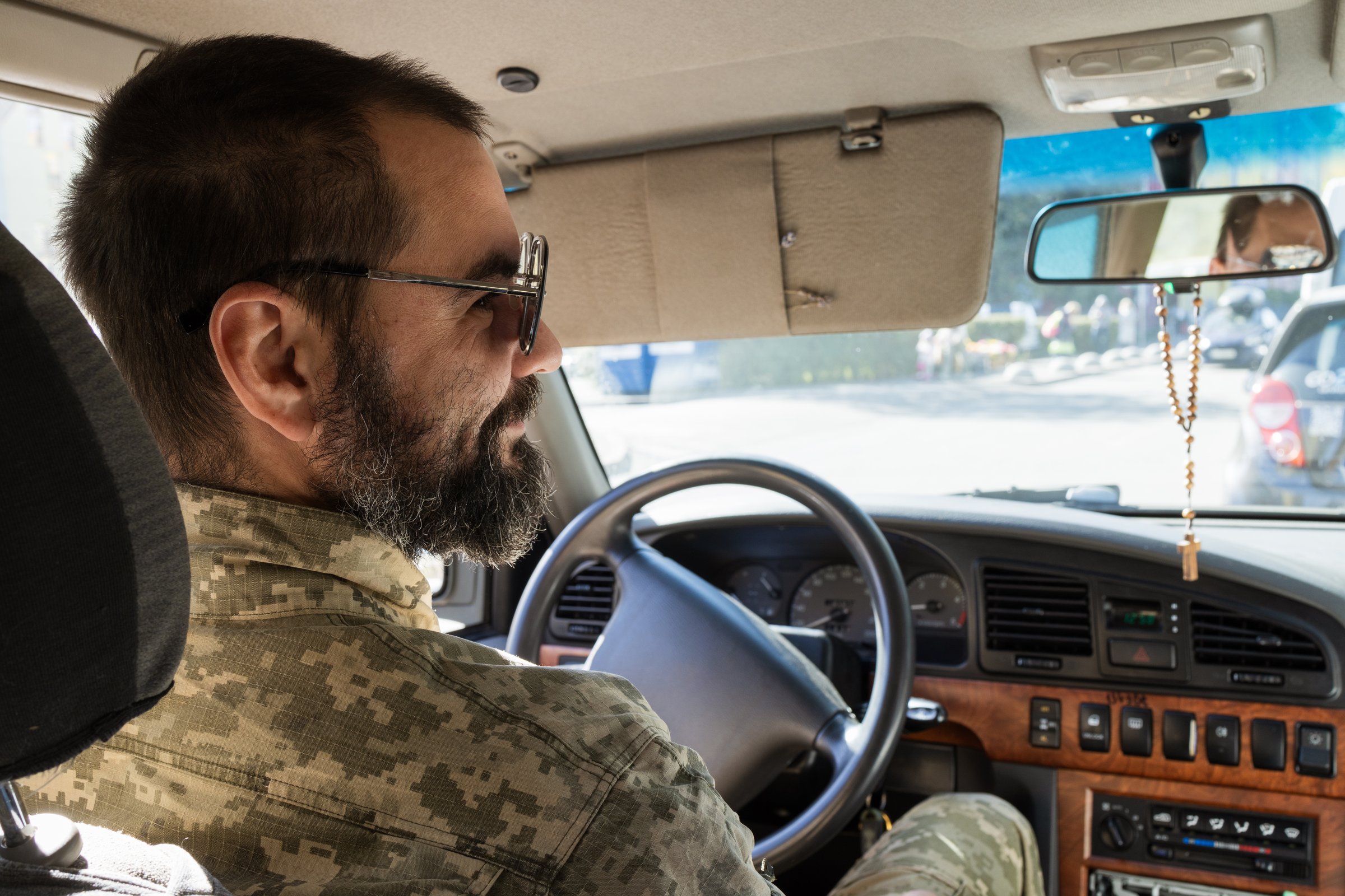 A Ukrainian soldier wearing sunglasses sits in a car and smiles