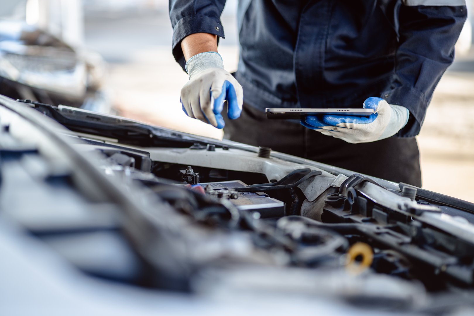Auto mechanic repairman using a digital tablet to check the condition of engine room in the garage before changing spare parts, checking the mileage of the car, maintaining service automobile car