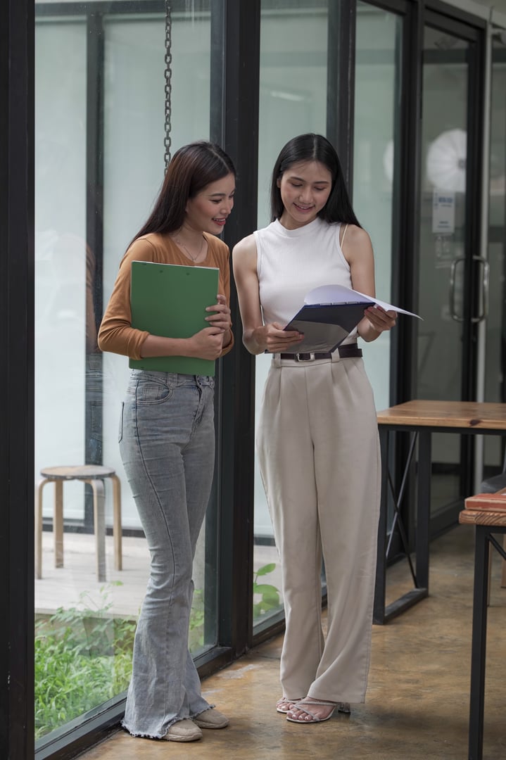 Two happy businesswomen talking and consulting working together in the office.