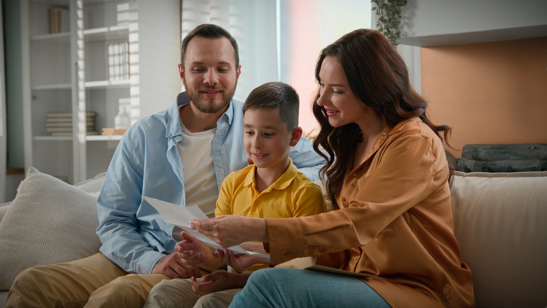 Happy Caucasian family mother father mom dad parents beloved son kid boy receive paper letter read good news together at home couch got invitation loan approval child accepted to school passing exam. High quality 4k footage