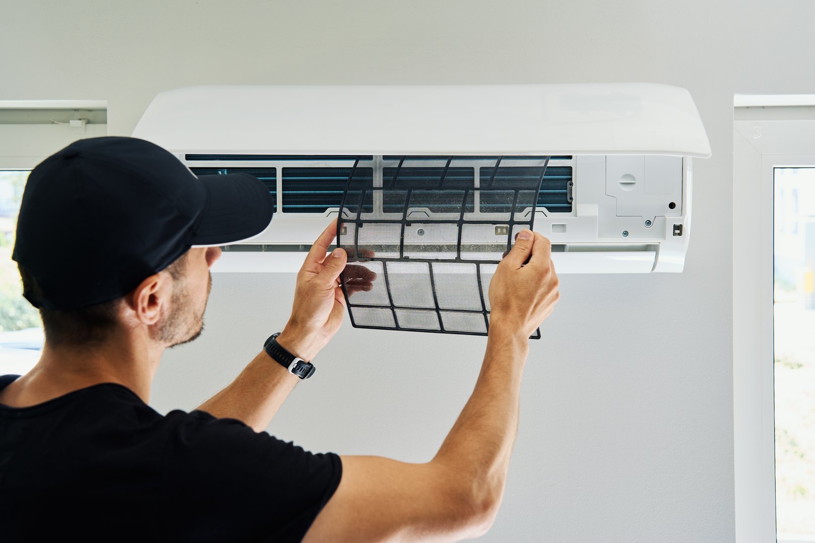 Air conditioner maintenance. Male technician repairs home climate system in living room. Man is cleaning filters of conditioner