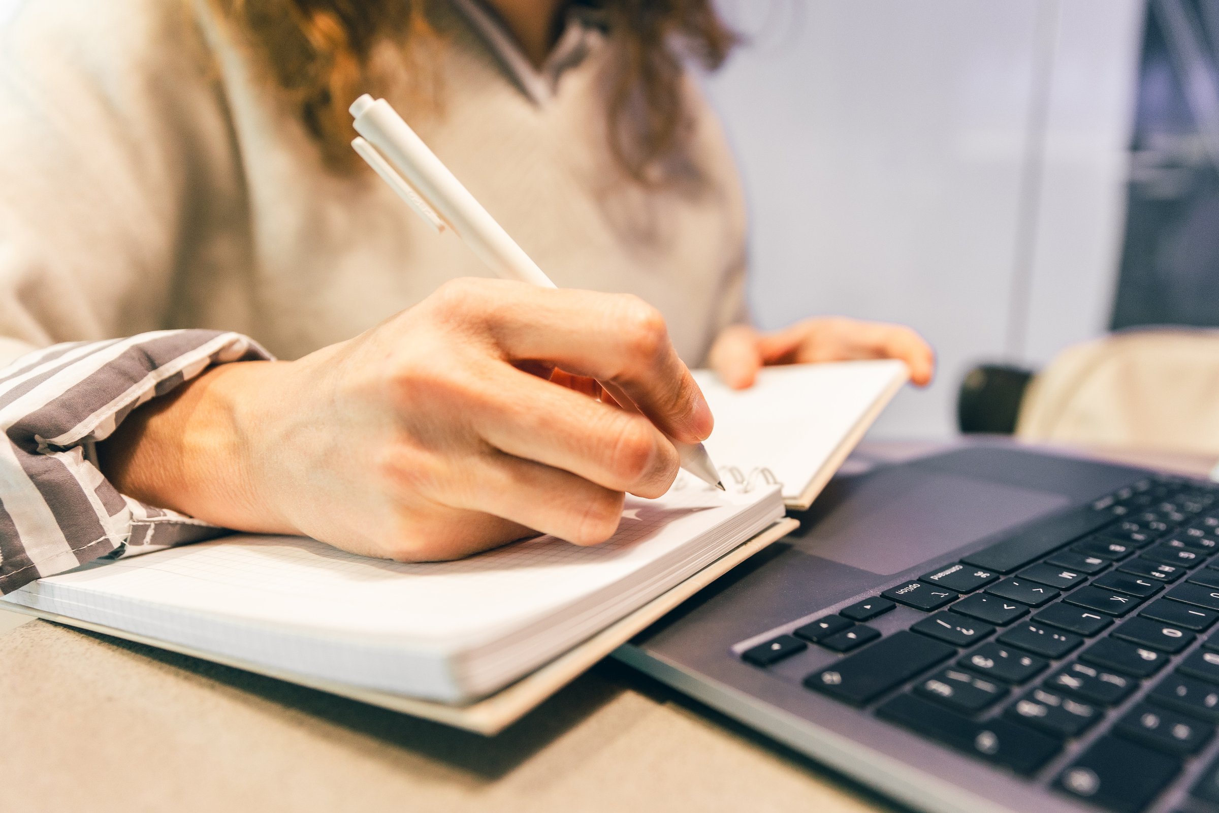 Professional woman writing notes in notebook next to laptop