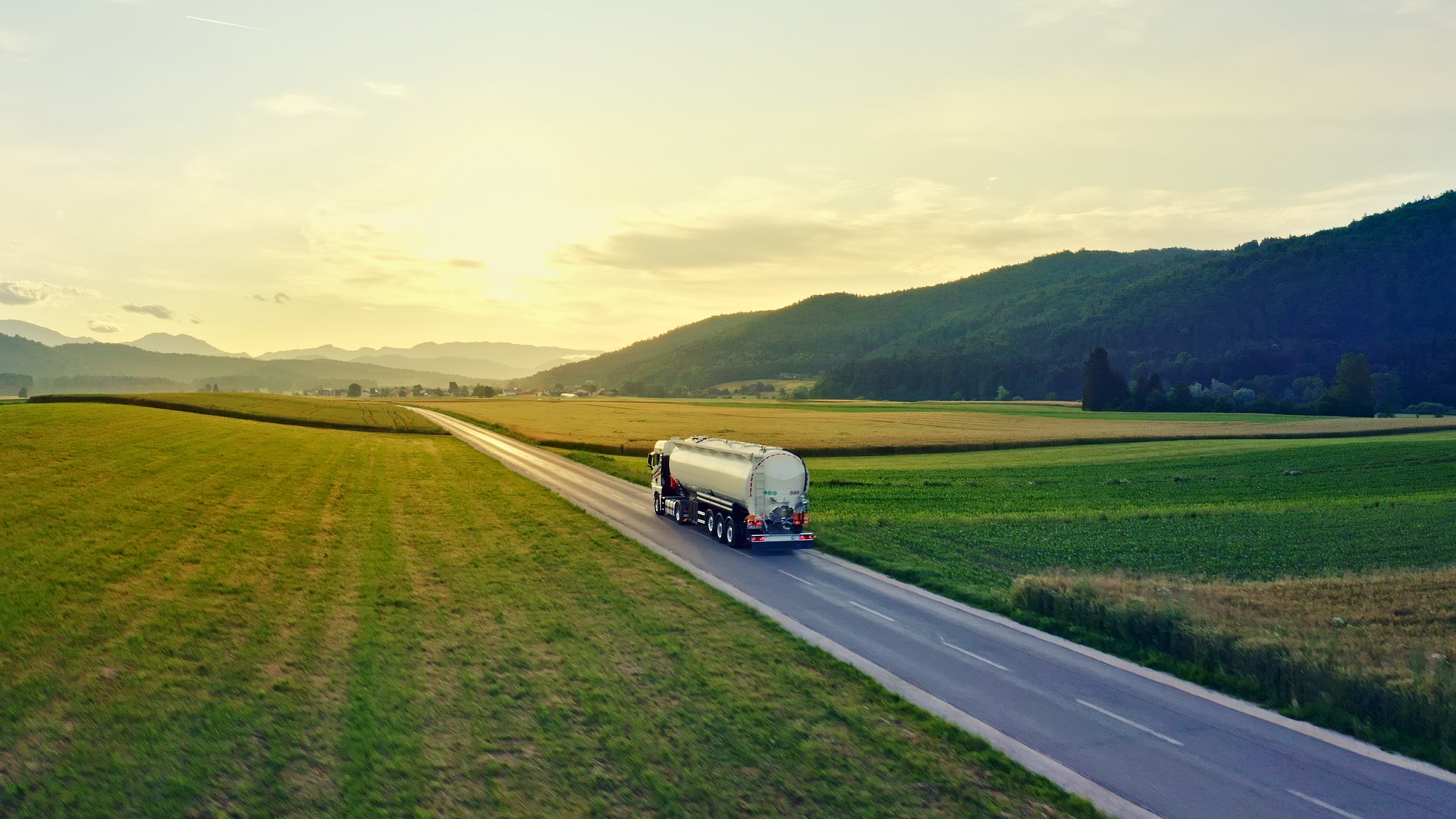 Aerial view of a tanker truck driving down a rural road, surrounded by vast fields and hills, symbolizing the vital role of transportation in cargo distribution.