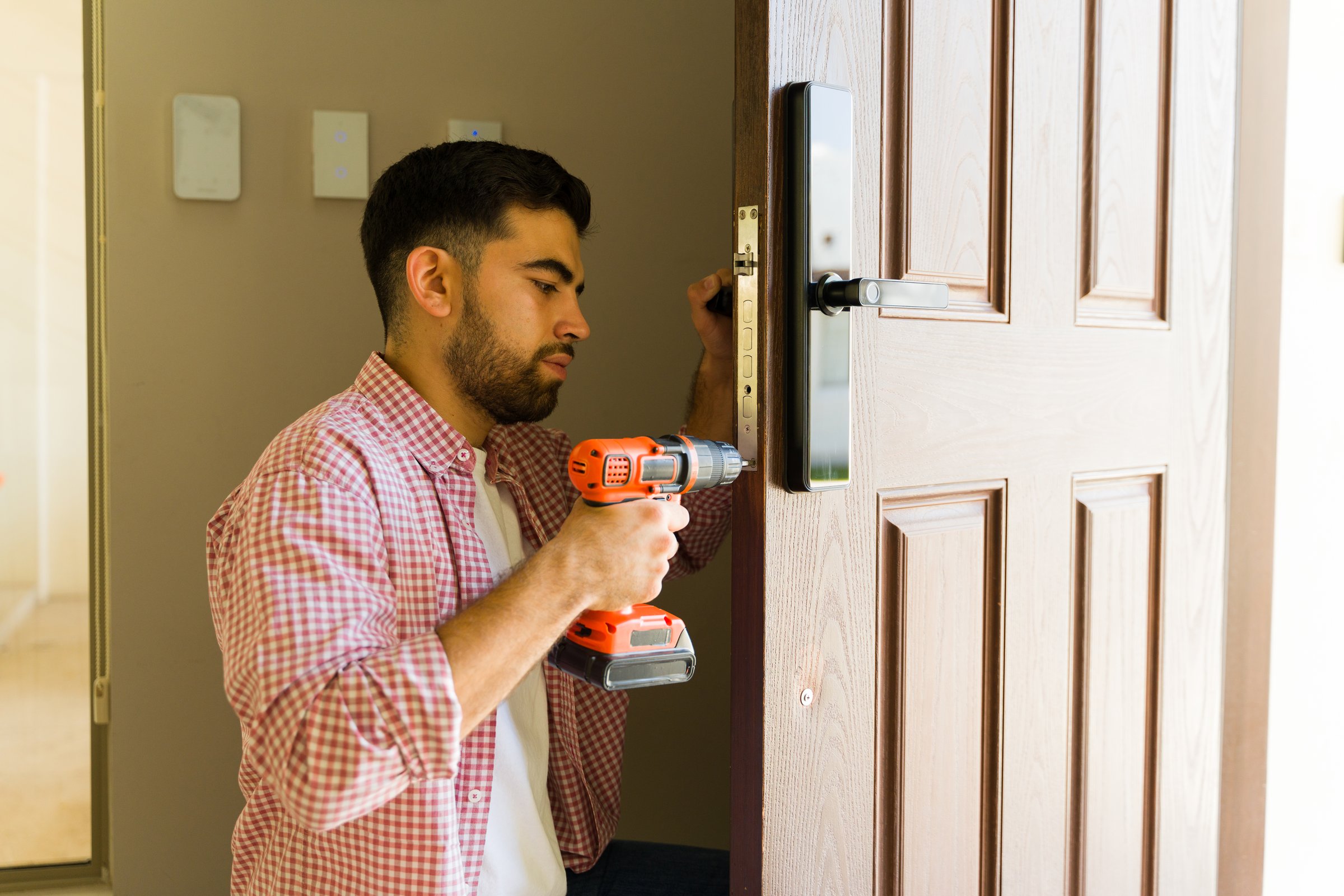 Experienced handyman is carefully installing a smart lock on a front door, using a screwdriver to ensure a strong and secure attachment