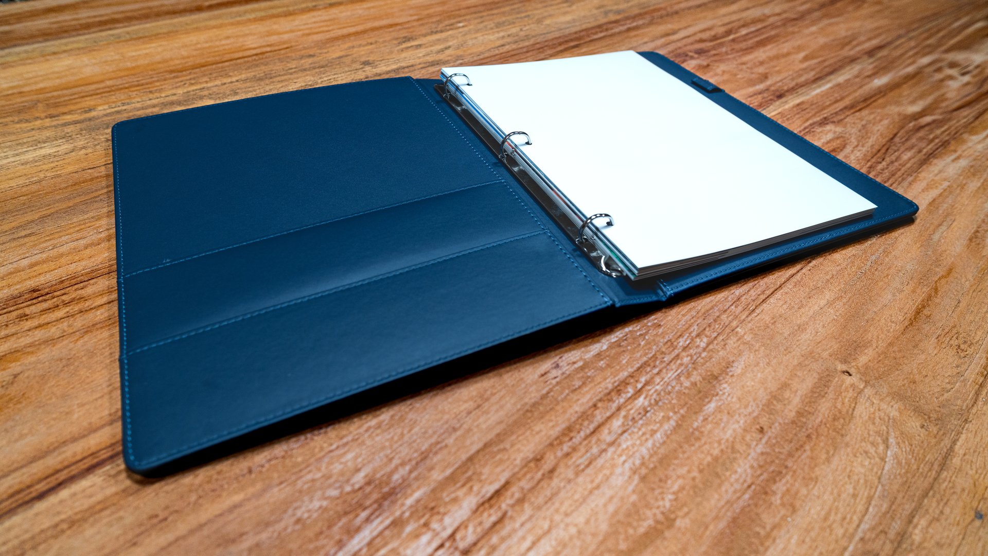 an open professional blue binder with blank white pages on a wooden surface.