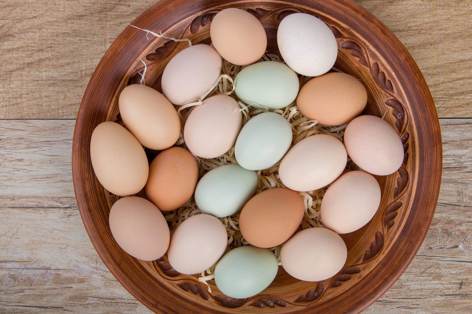 Eggs in a clay bowl on a wooden background. Top view. Multicolored eggs.
