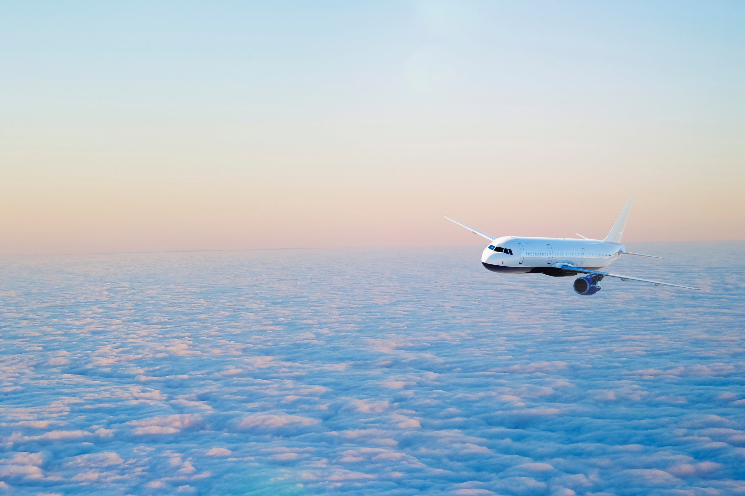 Airplane flying above a sea of clouds against a pastel sky at sunset or sunrise.