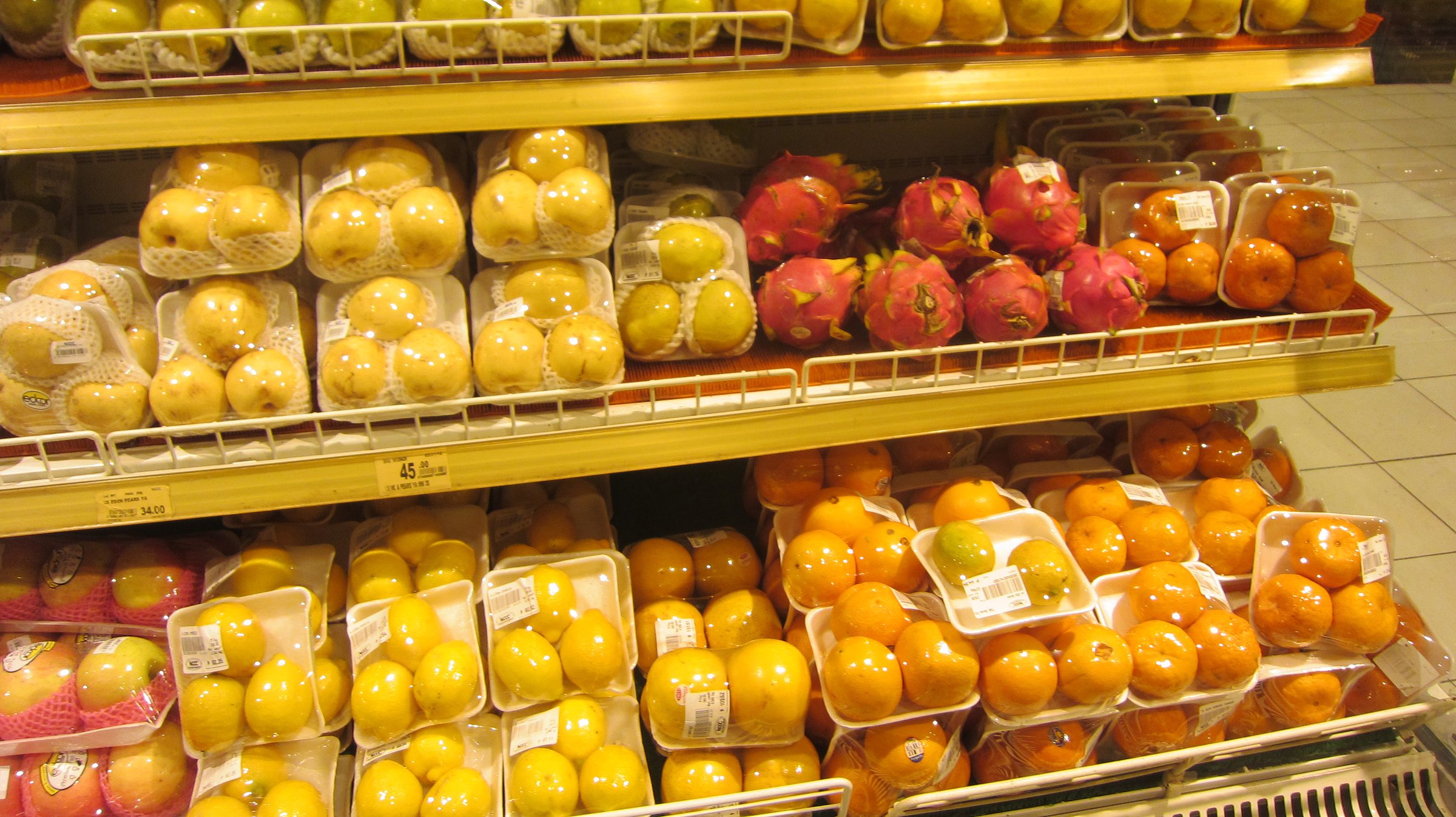 Packaged fruit display in a supermarket in Davao City, Philippines. Green apples, yellow pears, dragon fruits, and citrus varieties are arranged in plastic trays with barcode labels, reflecting urban food culture and tropical abundance. Davao City, Philippines on April 02, 2012