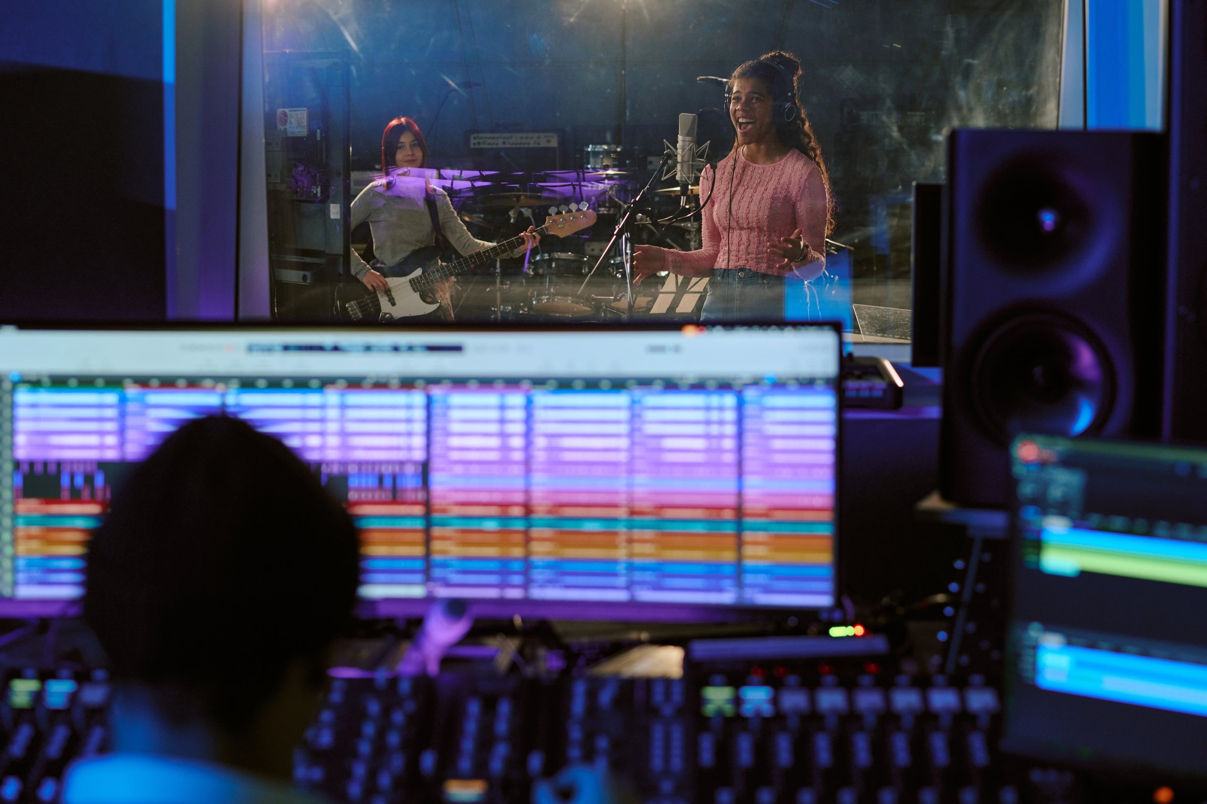 Talented girl band recording new album at professional studio, vocalist discussing details with sound engineer who working at digital audio workstation