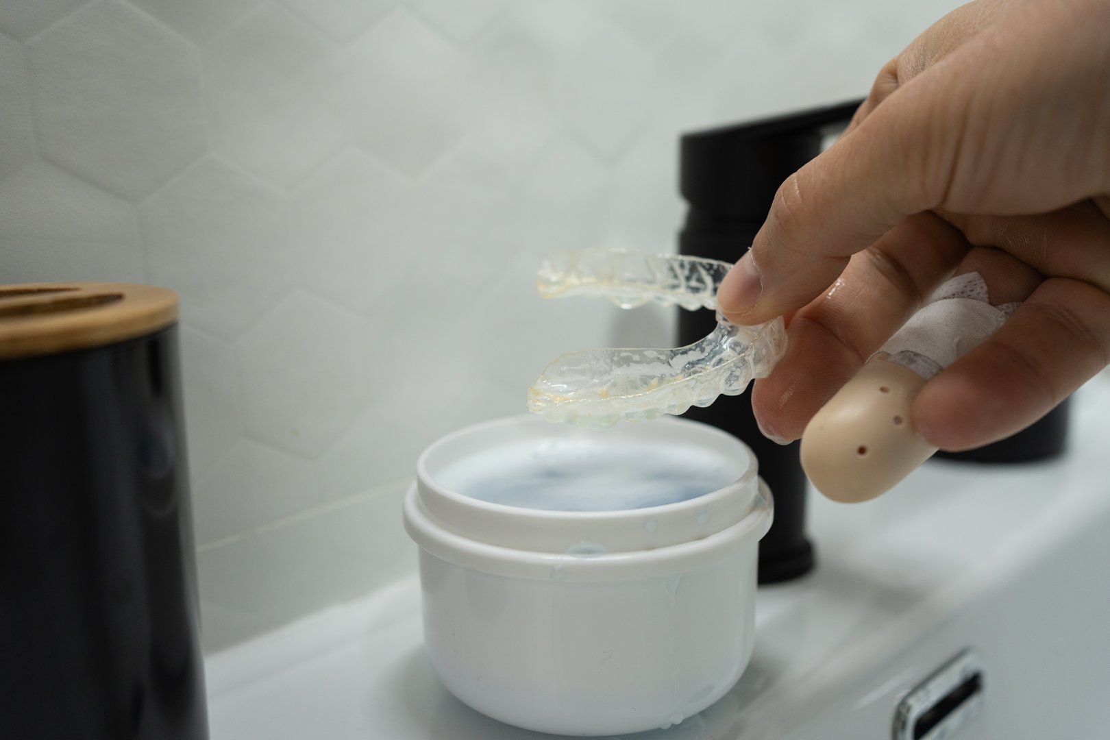 Close-up of unrecognizable man's hand placing used denture in plastic cleaning glass