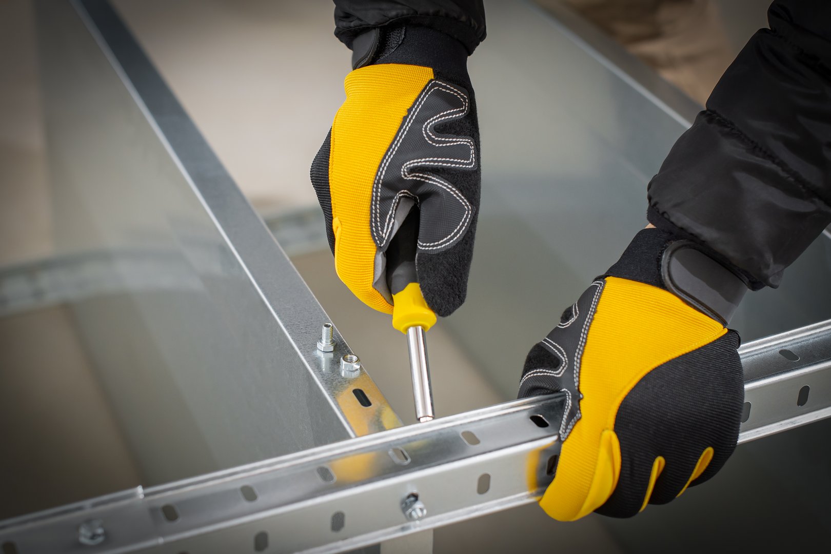 Worker hands in safety gloves mounting modular steel components with using screwdriver.