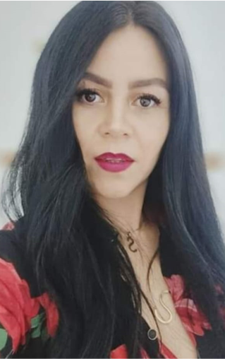 Woman with long black hair, wearing a patterned top, looks confidently at the camera.