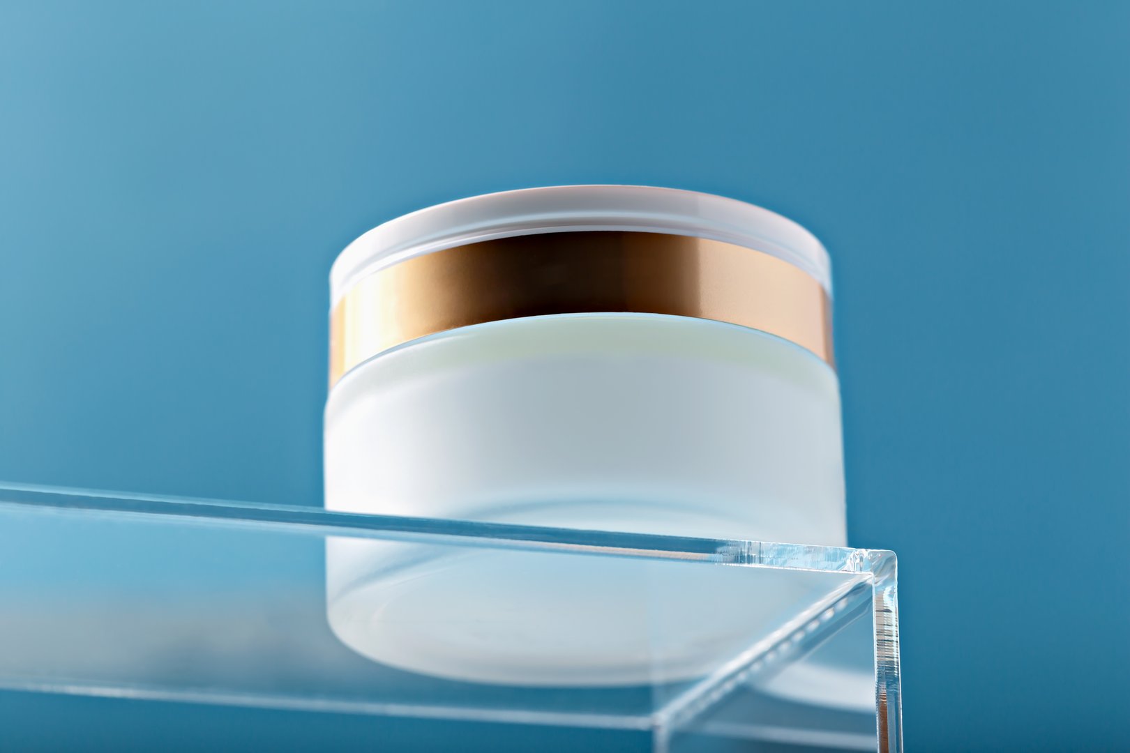 Mockup. Sleek cosmetic jar with gold accent featured on transparent surface against clean blue background, embodying luxury, minimalism and sophistication in branding for beauty and skincare products