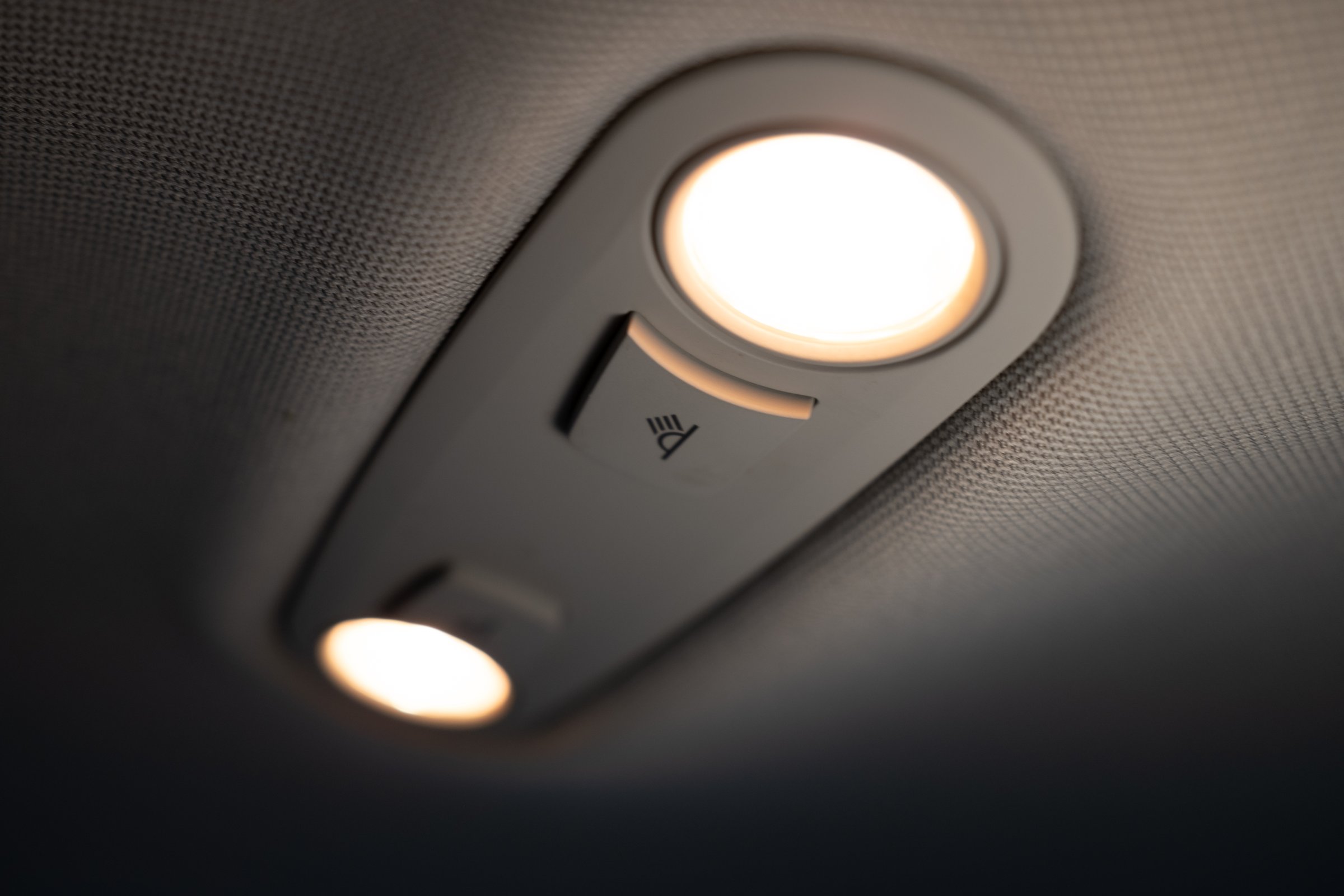 Close-up of a switched-on dome light in a car interior. Warm illumination inside the vehicle cabin. Selective focus on the lamp and switch on the ceiling.