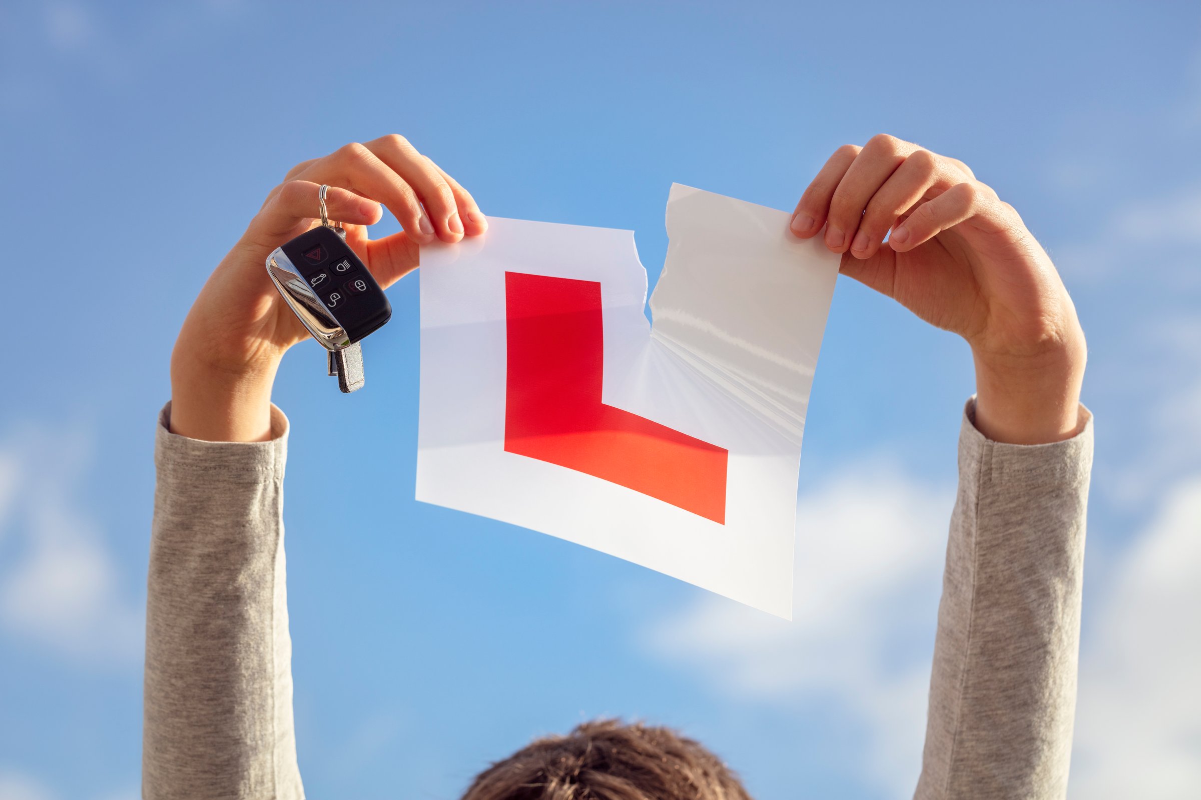 Tearing L plate against a sky holding a car key after passing driving test