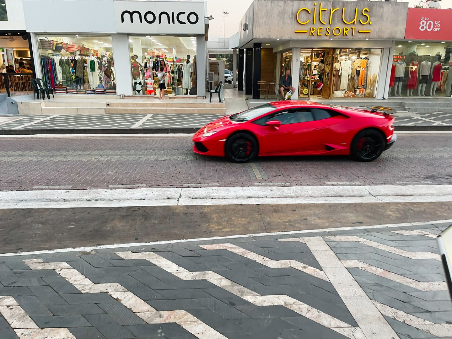 Paralimni, Cyprus - July 18, 2024: A bright red luxury Lamborghini Huracan car speeds along a stylish street beside boutique shops in Paralimni, Cyprus.