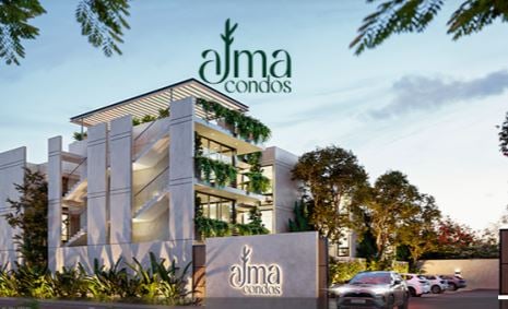 Modern building with greenery and Alma Condos signage, surrounded by parked cars and trees, under a clear sky.