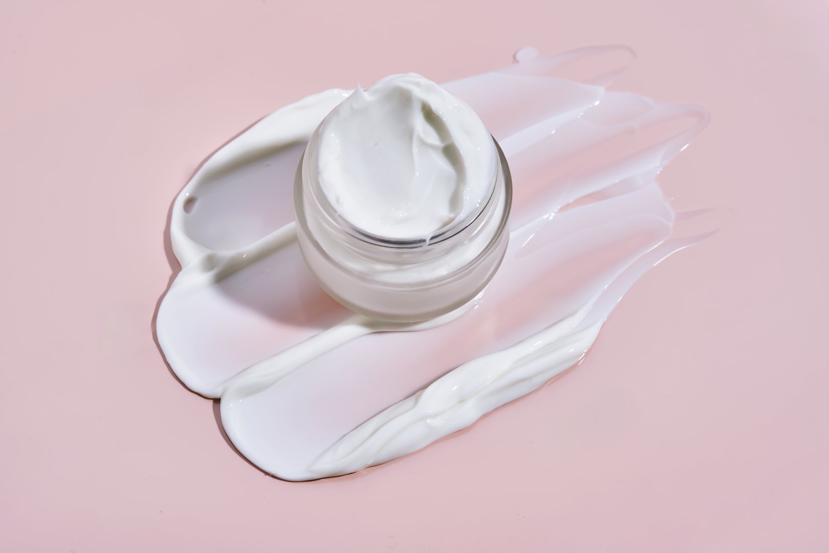 An open jar of cream with its texture on a pink background. High quality photo.