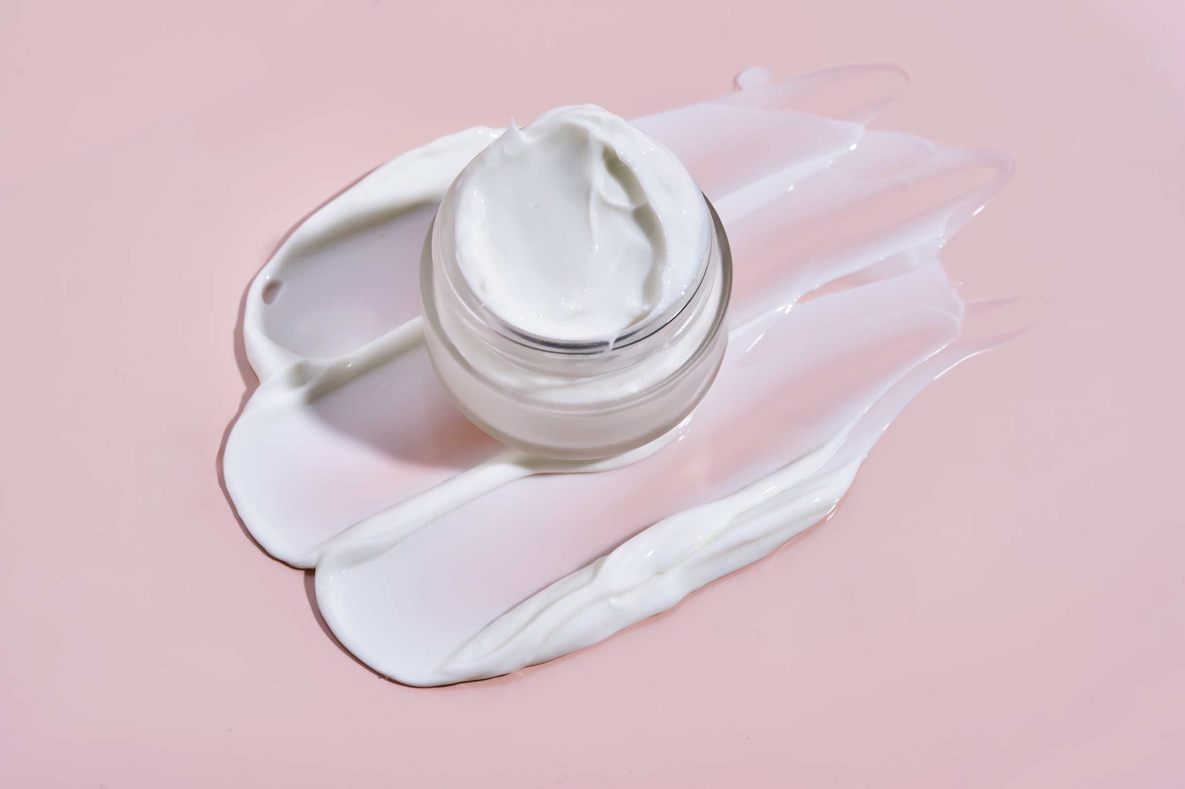 An open jar of cream with its texture on a pink background